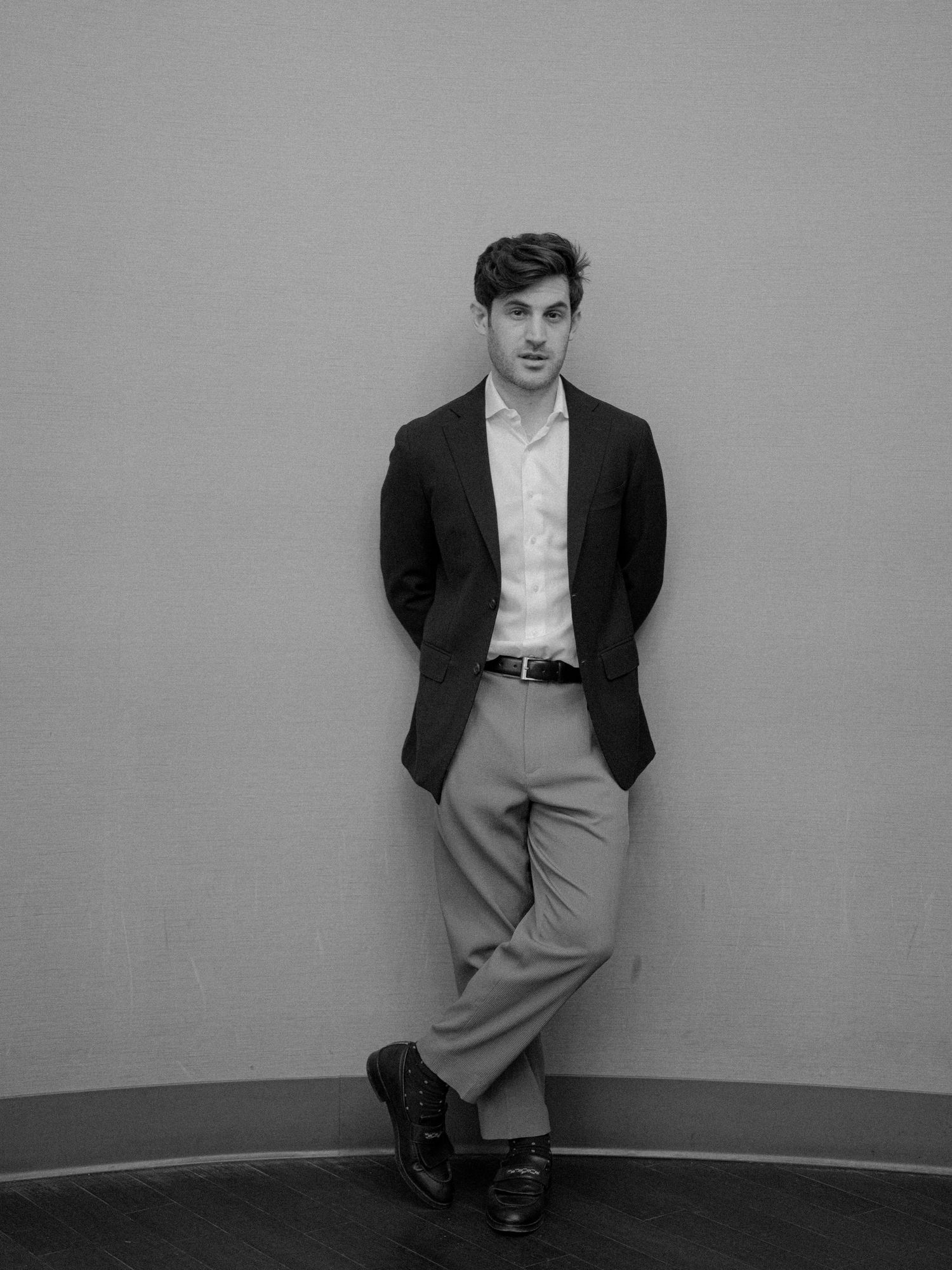 A person in formal attire leans against a curved wall in a classic black and white portrait.