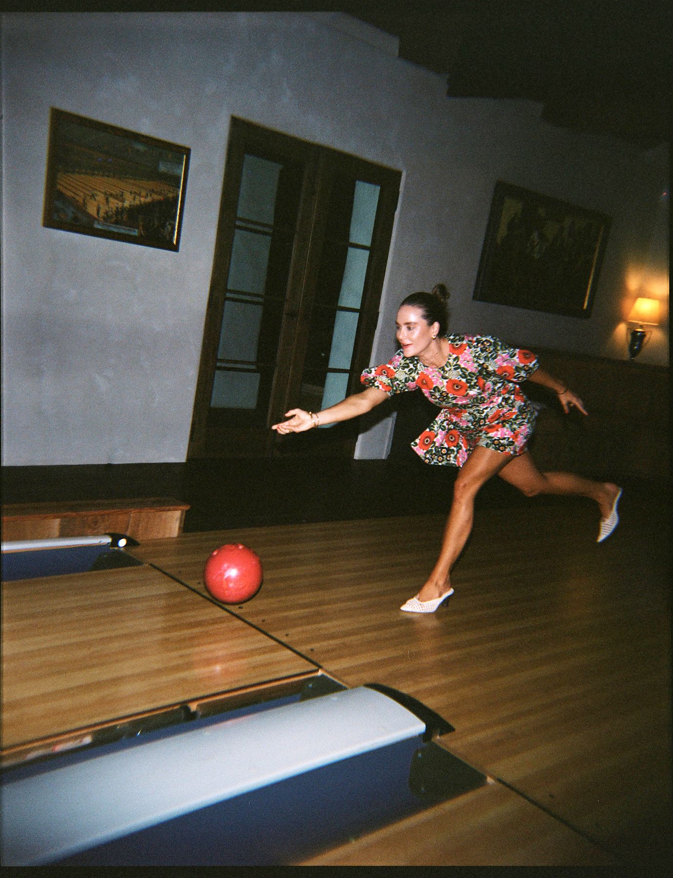 Person in colorful shirt bowling with red ball on wooden lane.