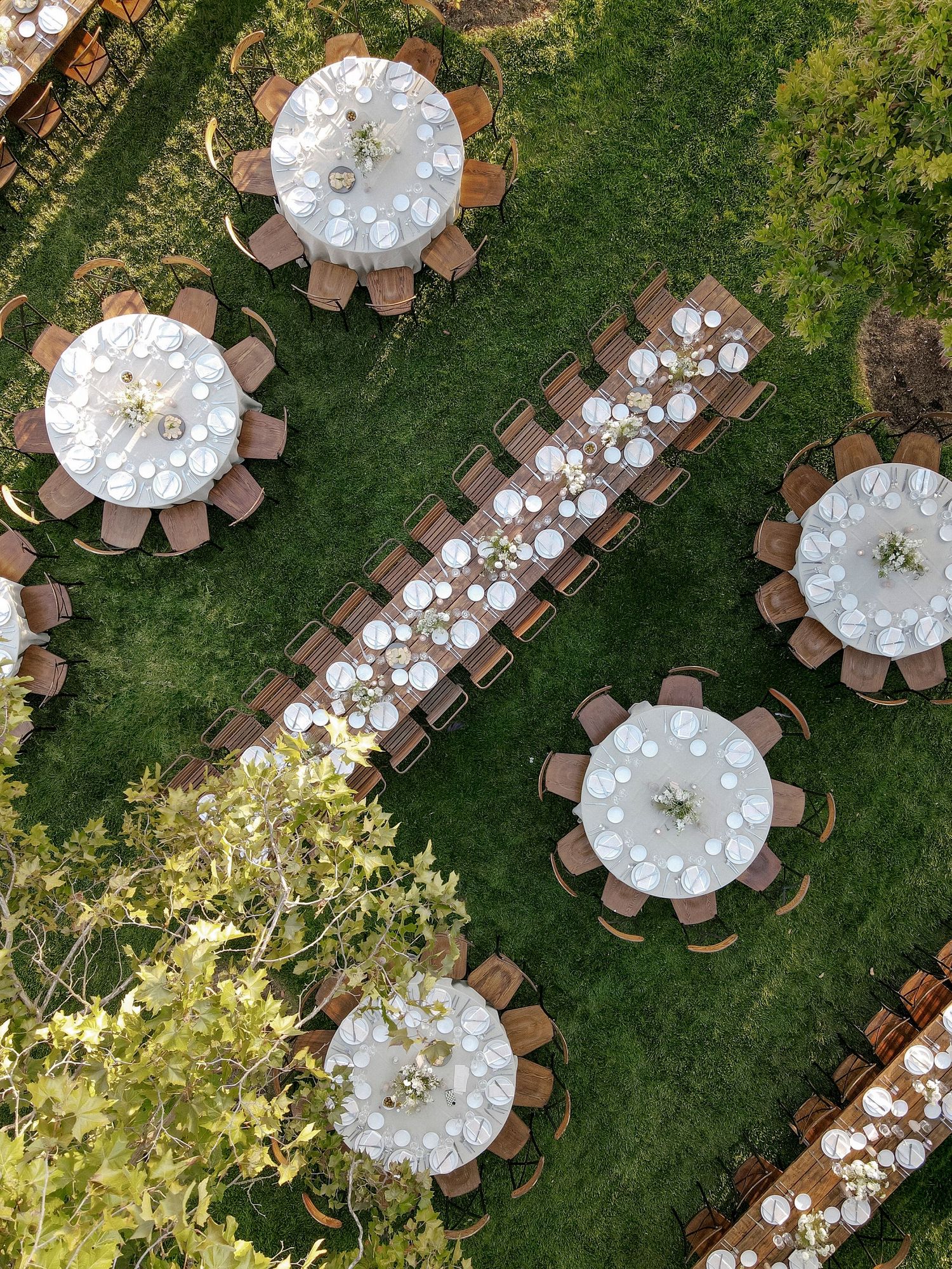 Aerial view of elegant round dining tables with white linens set up on a lush green lawn.