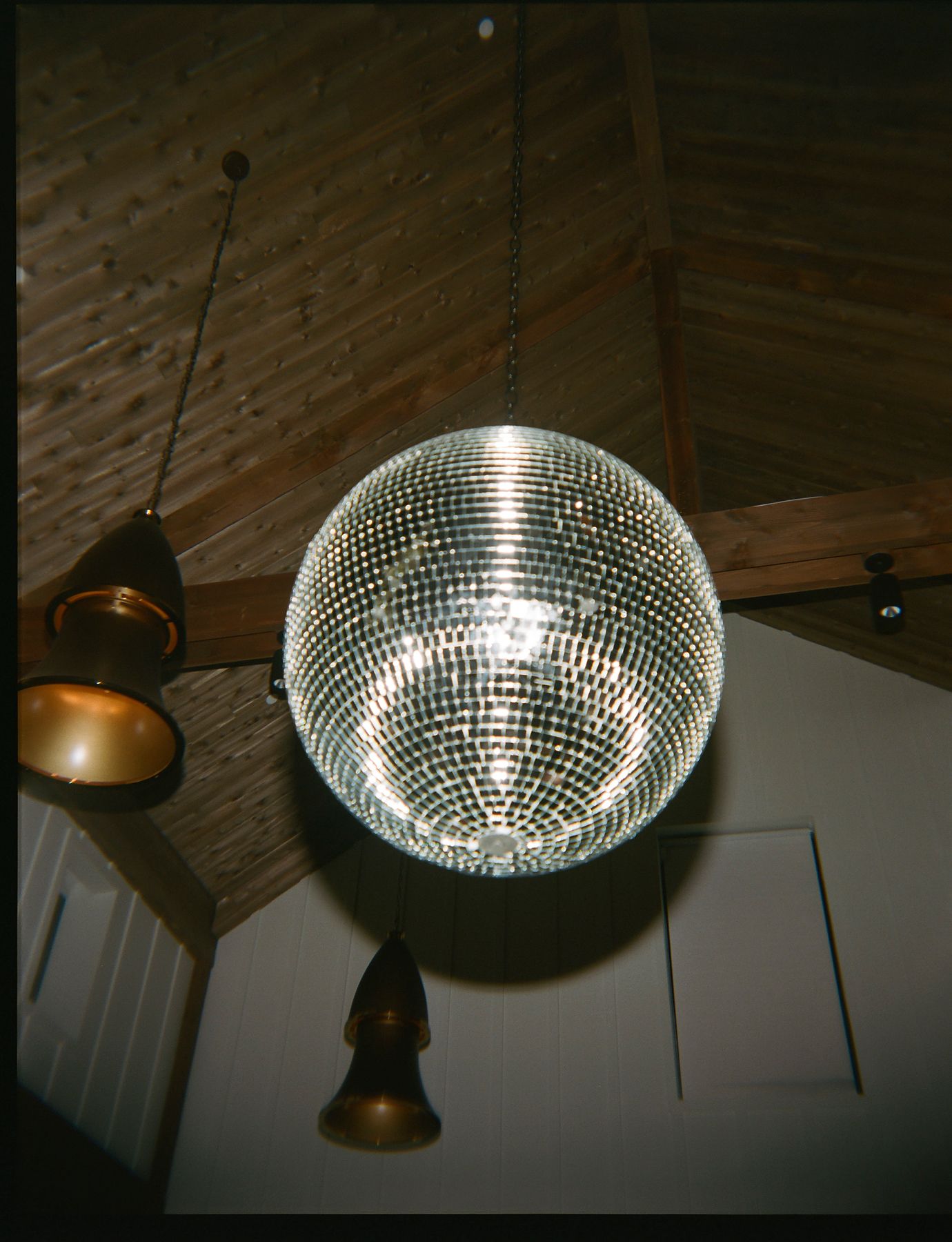 Disco ball hanging from wooden ceiling with pendant lights in dark room.