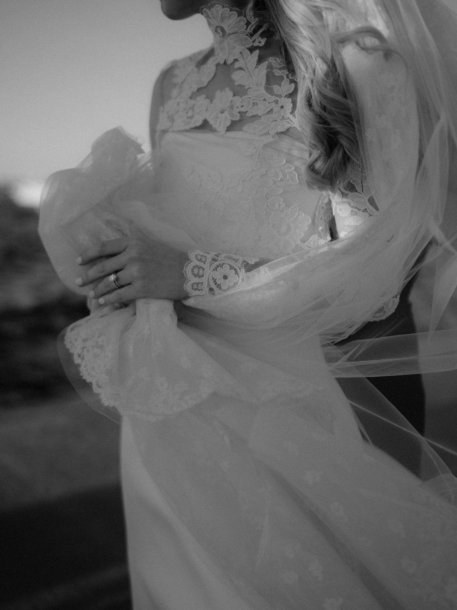 Black and white detail shot of a bride's lace wedding dress flowing in the wind.