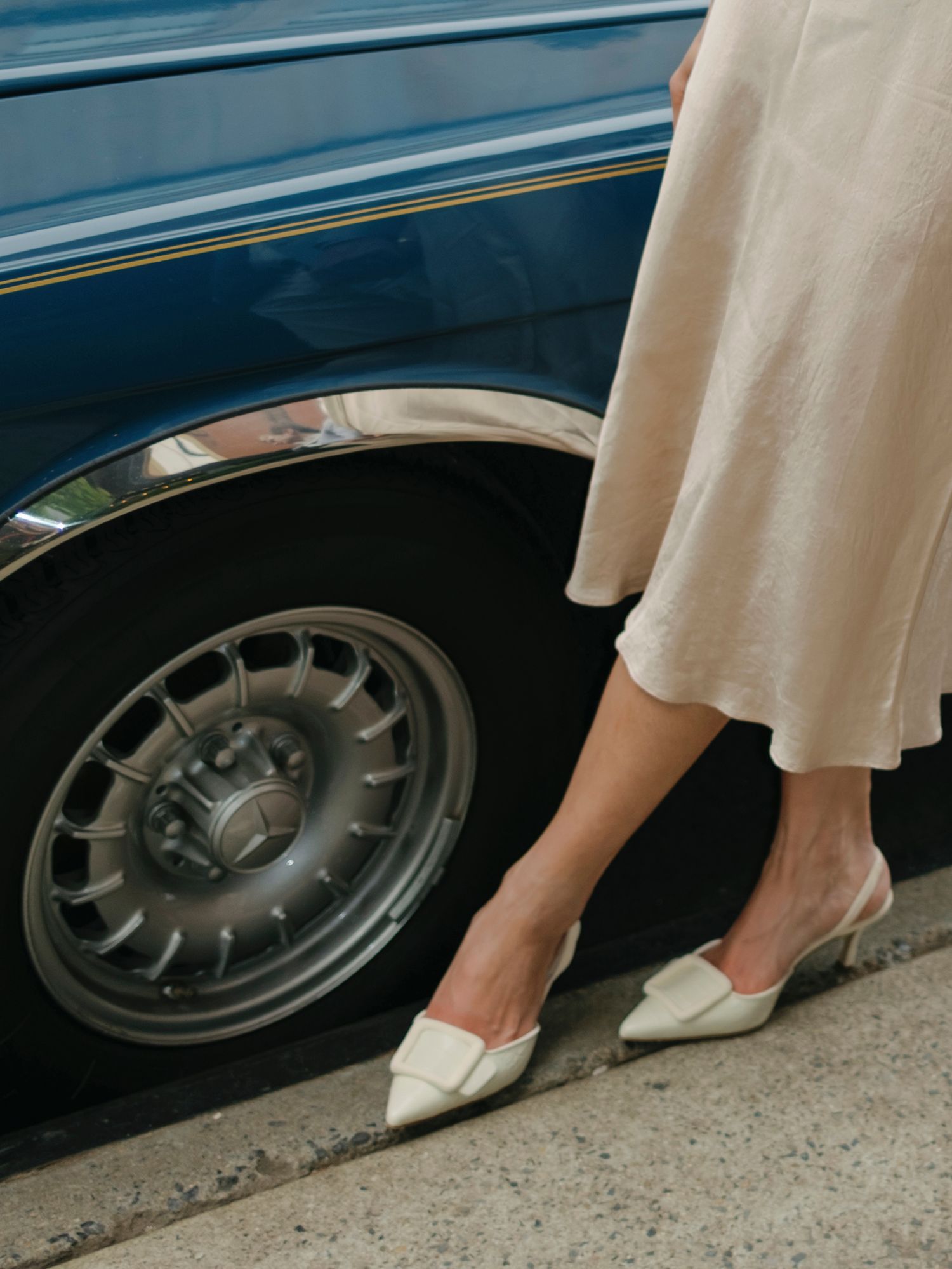 Close-up of white dress and heels against classic car wheel.