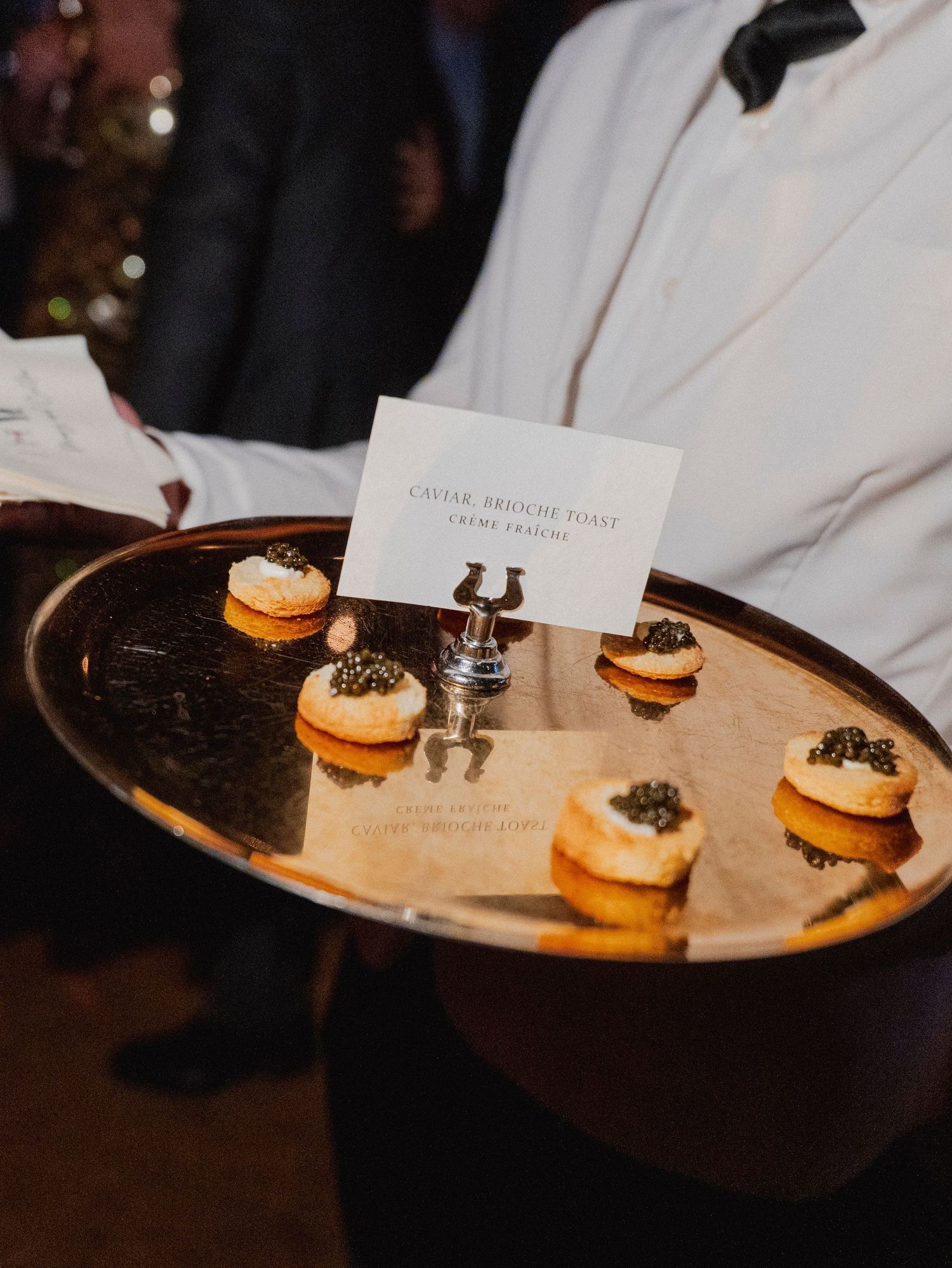 Small gourmet appetizers with caviar served on a golden tray with a place card.