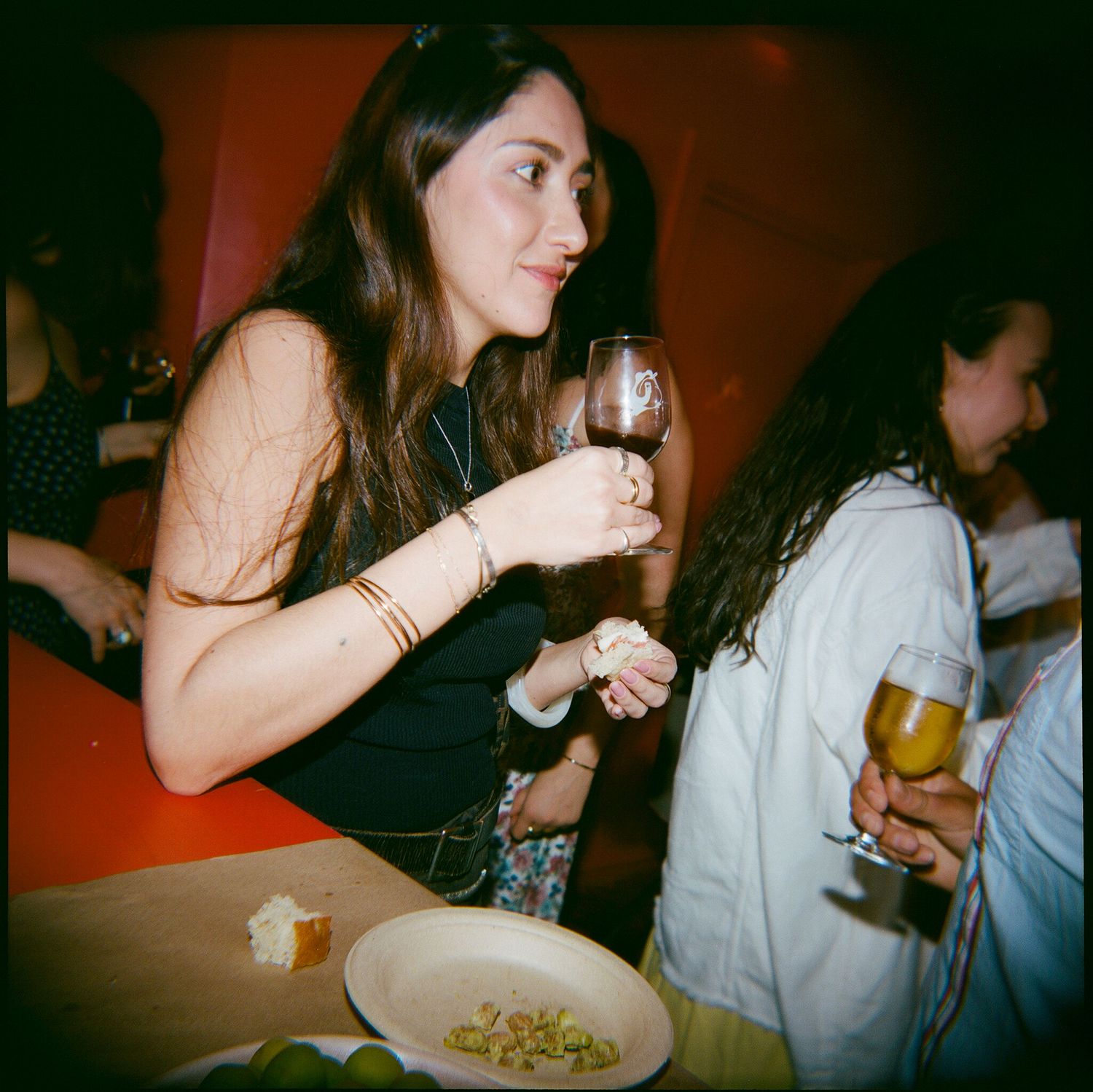 Friends gathered around a table enjoying wine and snacks in dim lighting.
