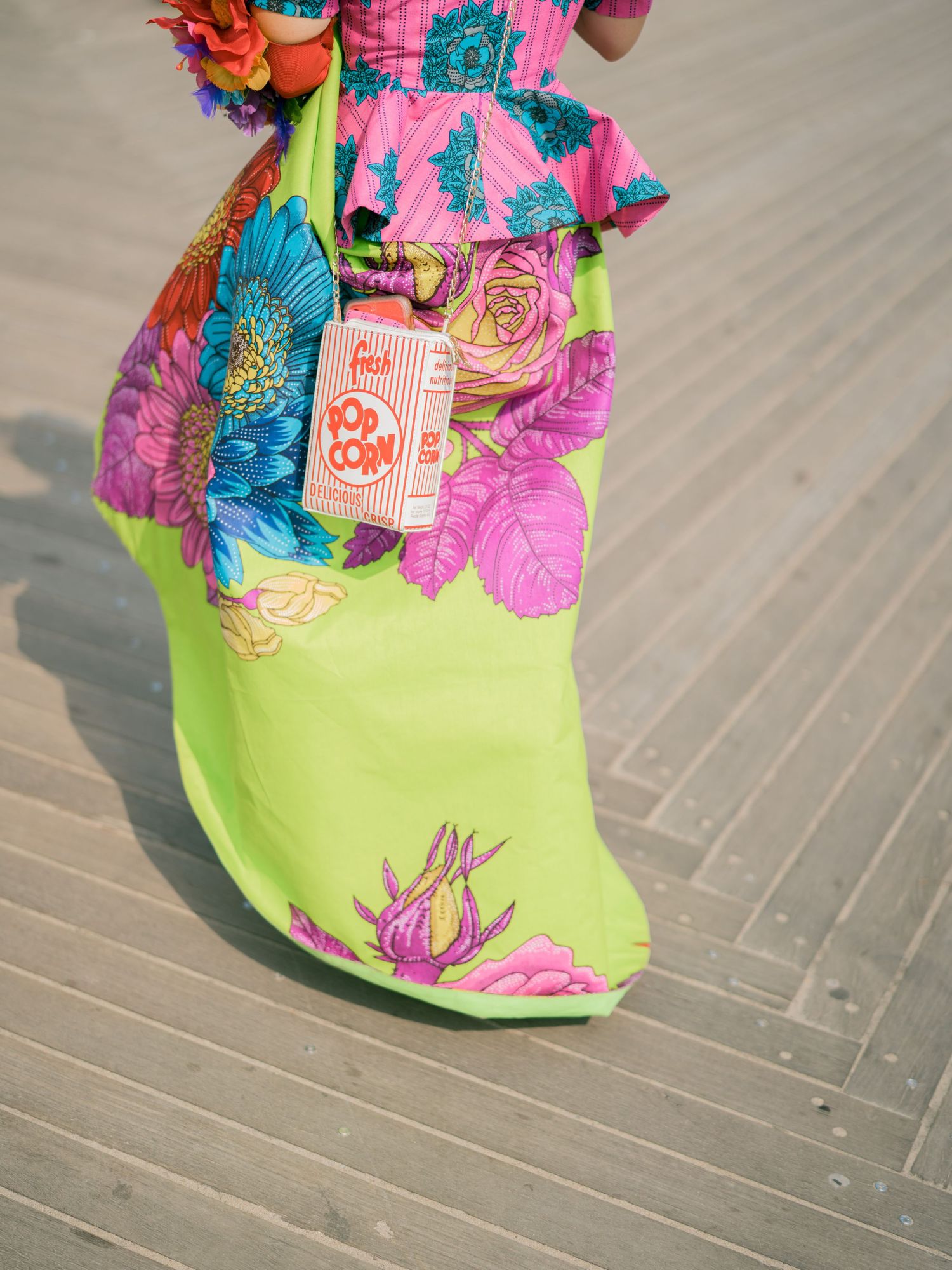 Close-up detail of a lime green dress with pink and purple floral embellishments on wooden boardwalk.