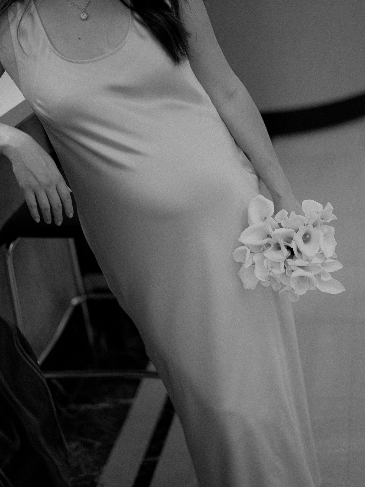 A close-up view of a sleek white dress with white calla lilies held at the side.
