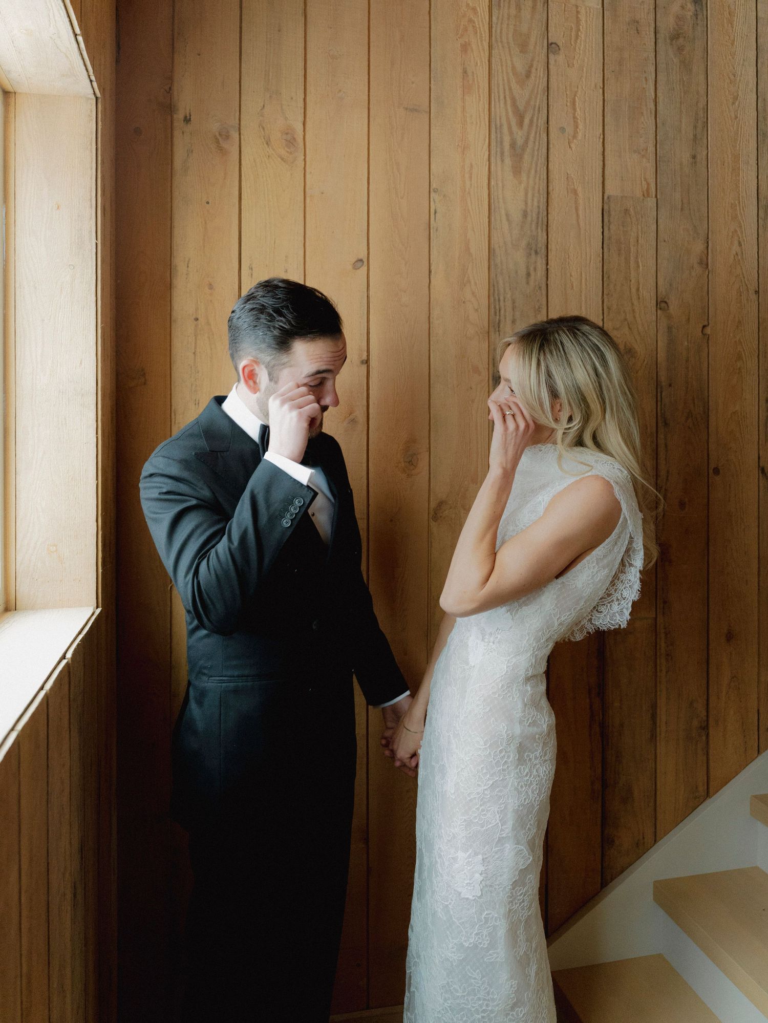 A couple shares a private first look moment in a rustic wood-paneled room.