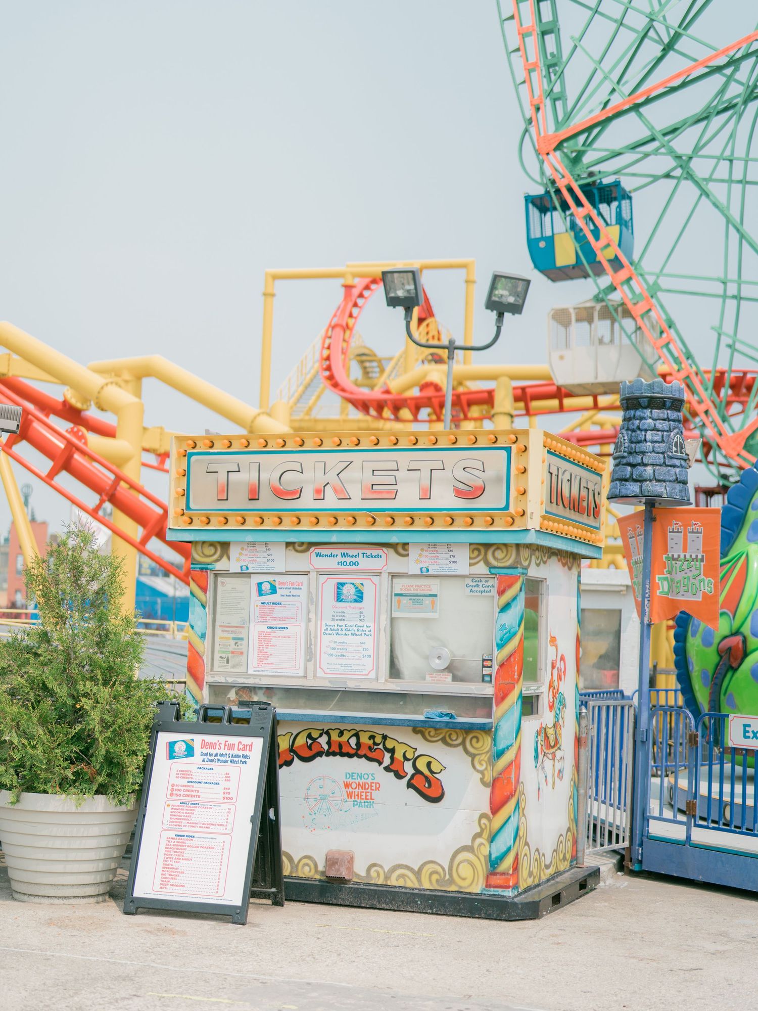Carnival rides and ticket booths with retro designs against a pale blue sky.