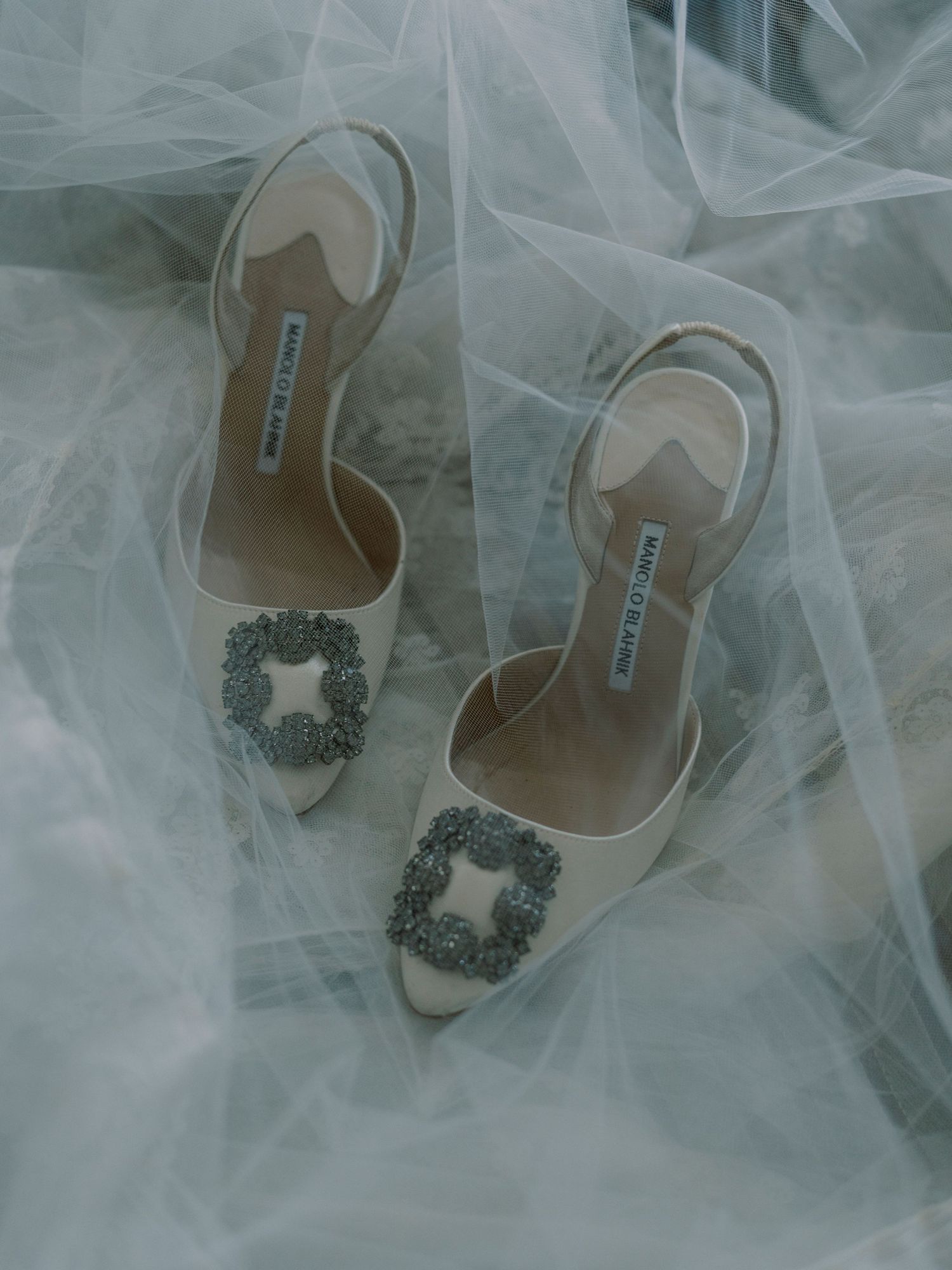 Elegant bridal shoes with crystal embellishments surrounded by tulle fabric.