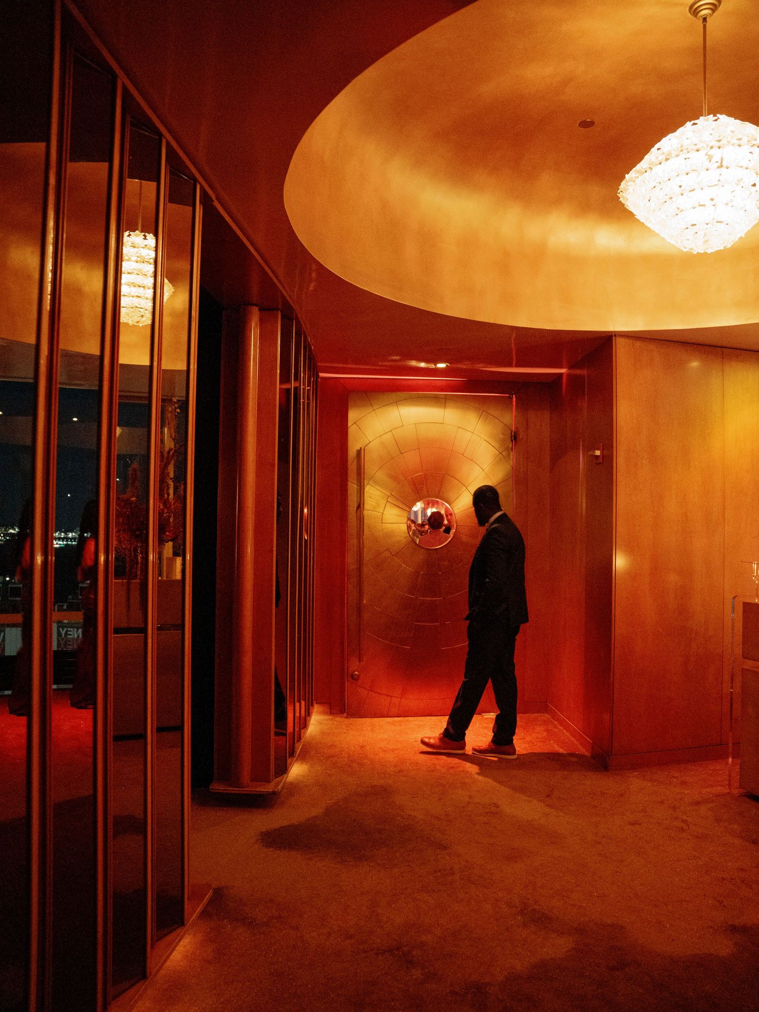 A silhouetted figure in a warmly lit, luxurious hallway with curved architectural details.