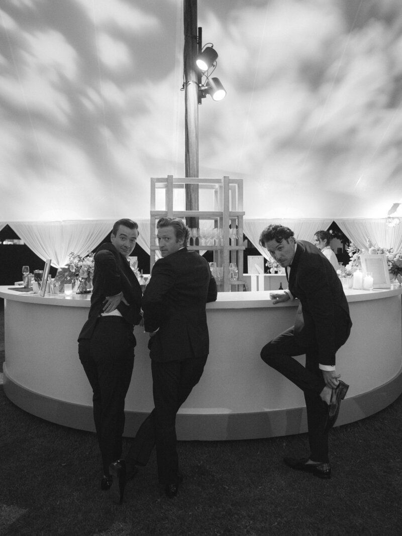 Three people socializing at a curved white bar under moody lighting.
