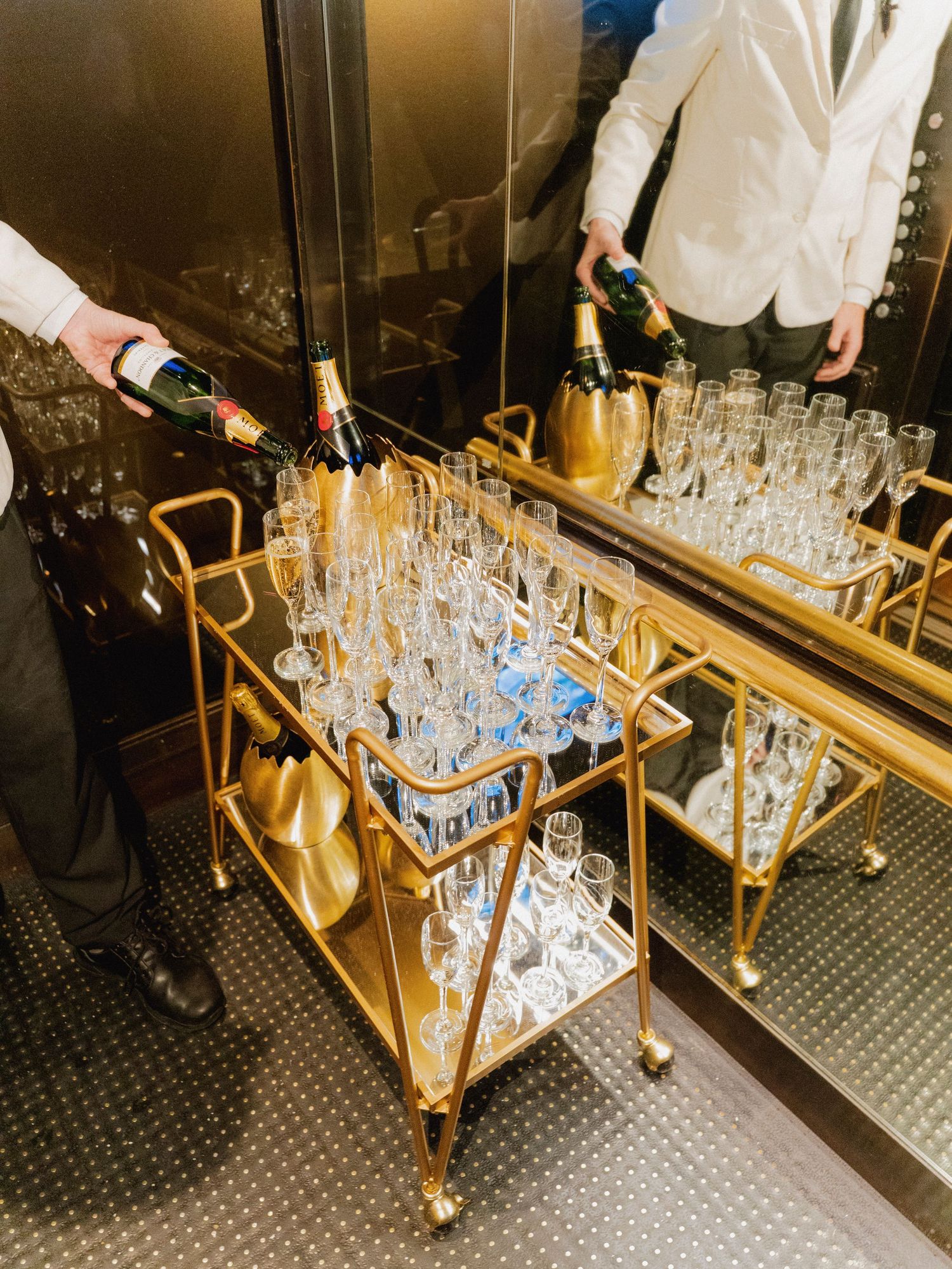 Gold bar cart filled with champagne glasses being prepared for service.