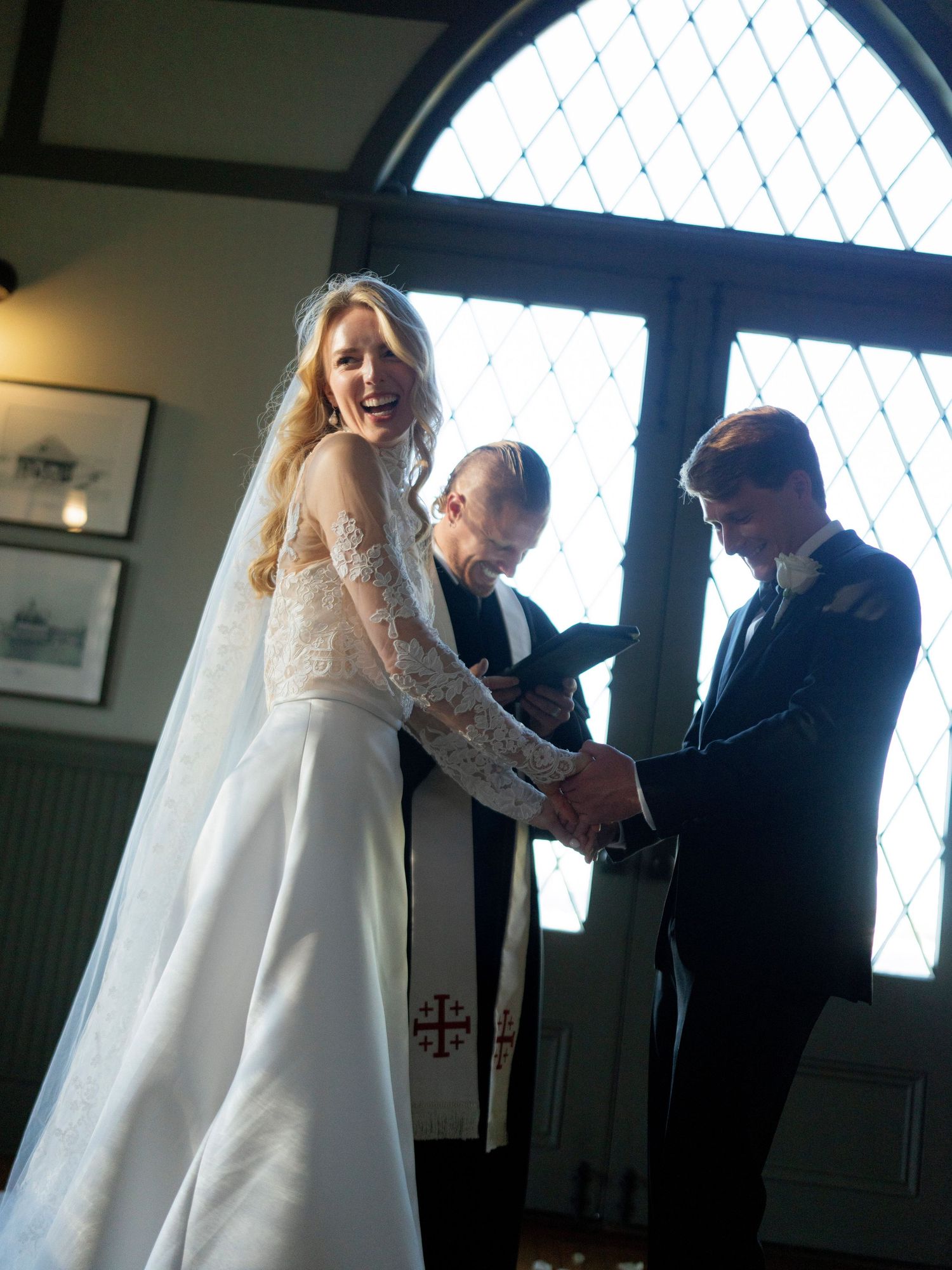 Backlit wedding preparation scene through latticed windows showing final dress adjustments.