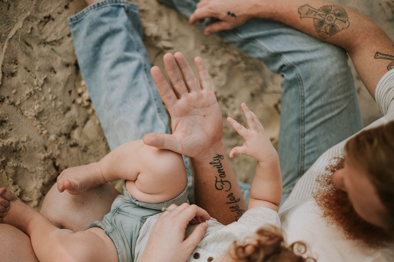 Close-up of hands and sandy feet on beach during family photo session.
