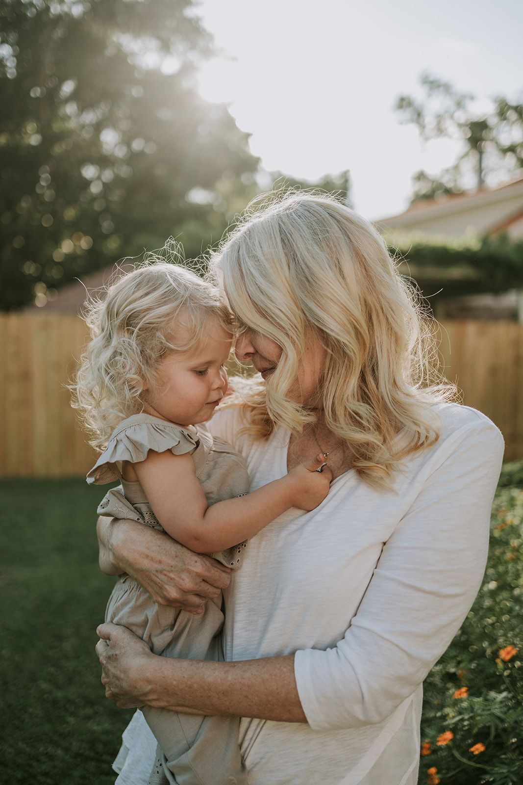 Tender embrace between parent and child in a sunlit backyard garden setting.