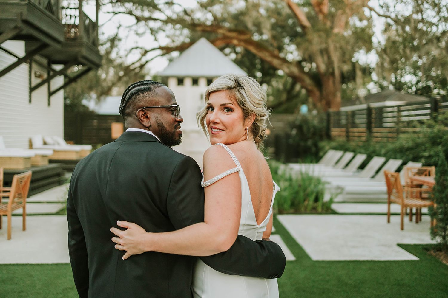 A couple shares an intimate moment during their outdoor wedding at a venue with lush greenery and white decor.