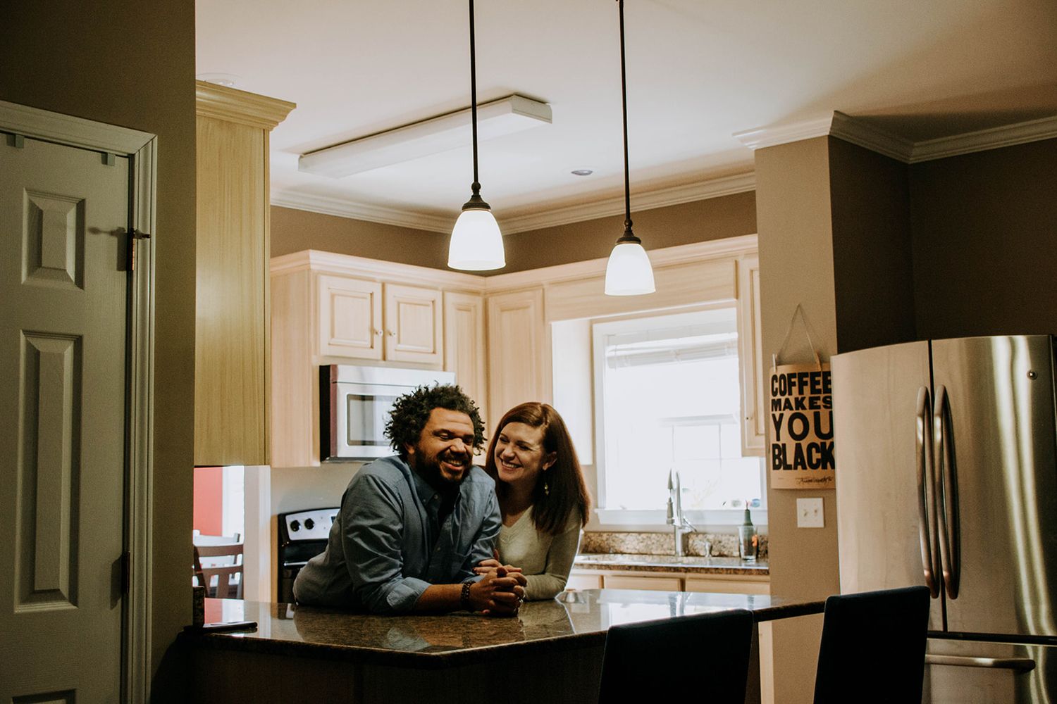 Cozy kitchen scene with couple laughing together at marble counter.