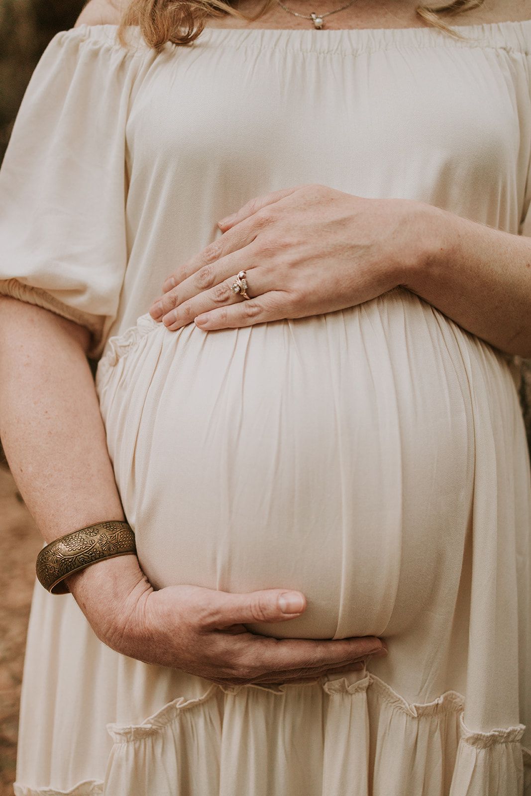 Close-up of hands gently cradling a pregnant belly in a flowing white dress.