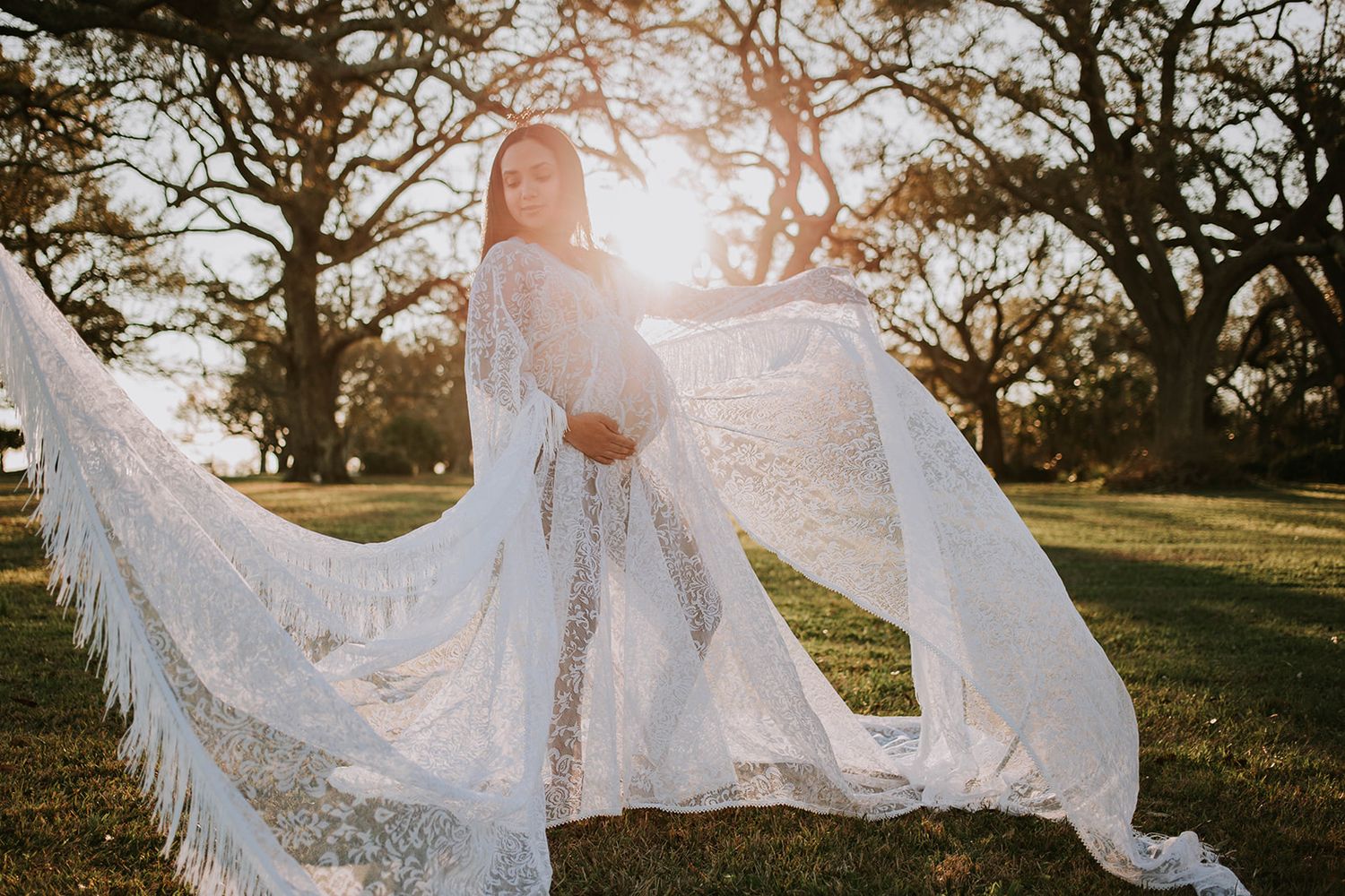 Flowing white lace maternity gown catches sunlight as fabric billows in outdoor golden hour photo.