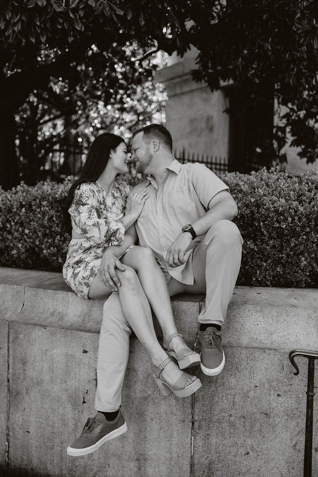 A couple sits close together on a stone wall in a romantic black and white composition.