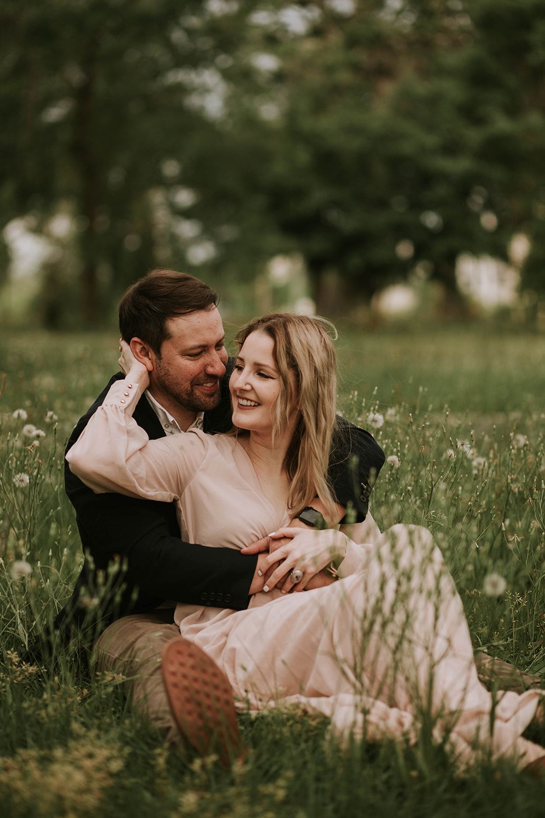 A romantic couple shares an intimate moment in a field wearing elegant spring attire.