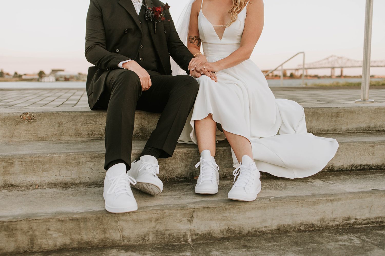 Wedding couple wearing matching white sneakers sitting on concrete steps in casual modern style.