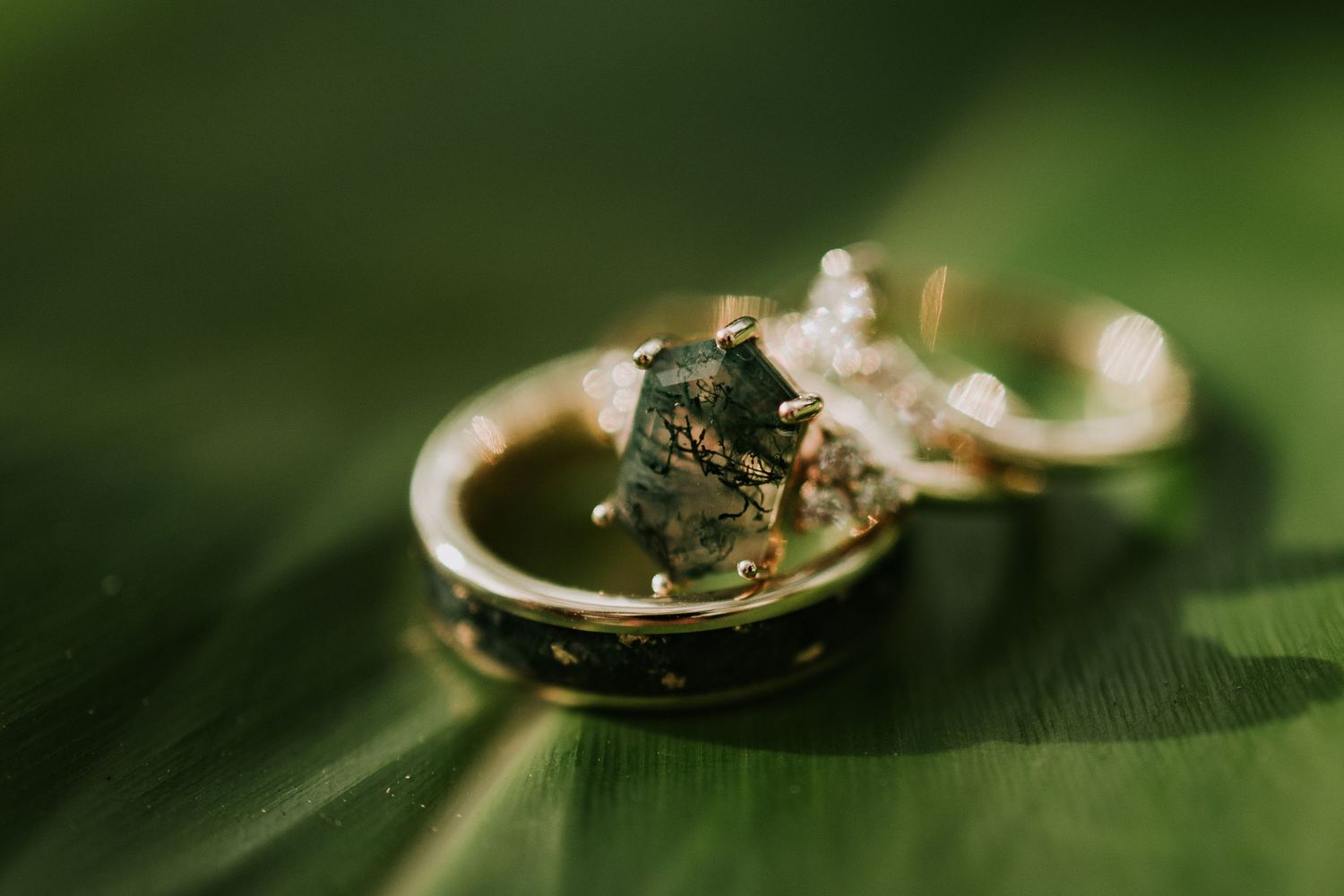 Gold engagement ring with green moss agate stone resting on a tropical leaf.