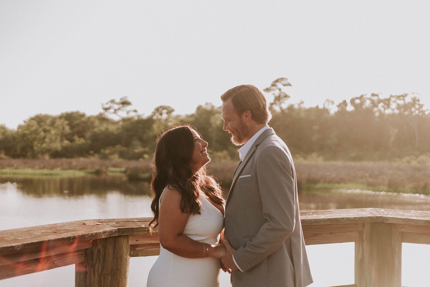 A couple shares a romantic moment at sunset on a wooden dock overlooking a serene waterway.