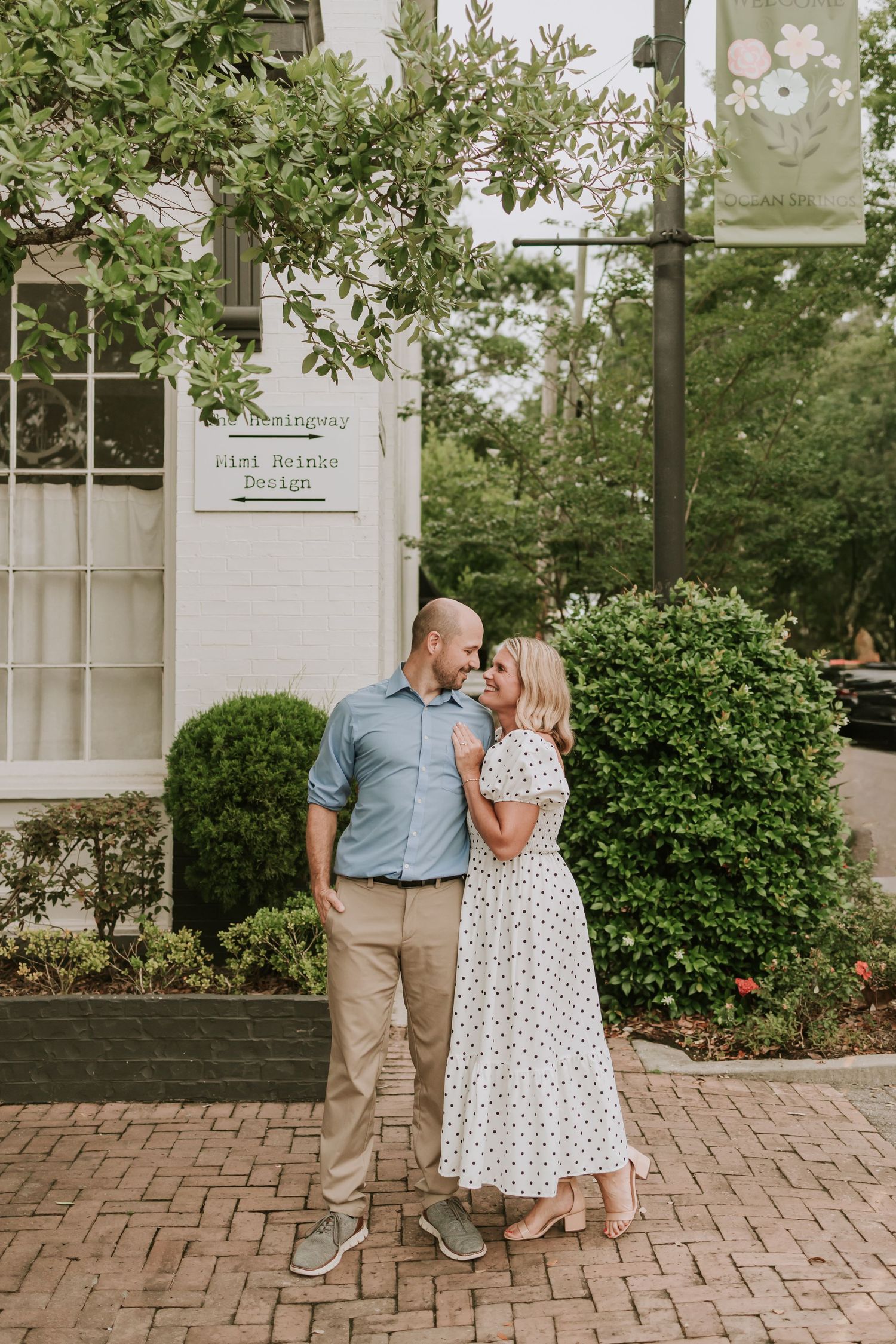 Couple sharing a romantic moment on a brick pathway outside a charming boutique shop surrounded by lush greenery.