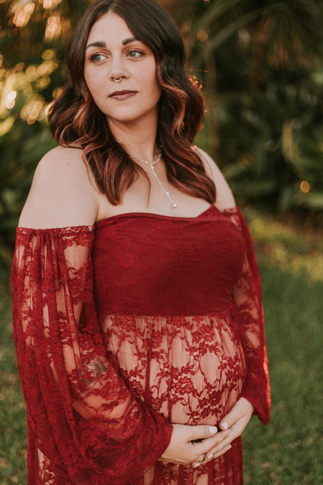 Close-up portrait showing burgundy lace maternity dress against sunset-lit foliage.