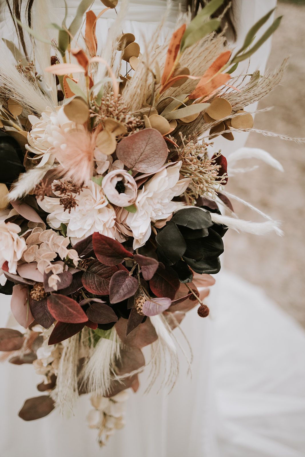 Elegant boho wedding bouquet featuring dried pampas grass, coral stems, and muted roses in cream and dusty pink tones.