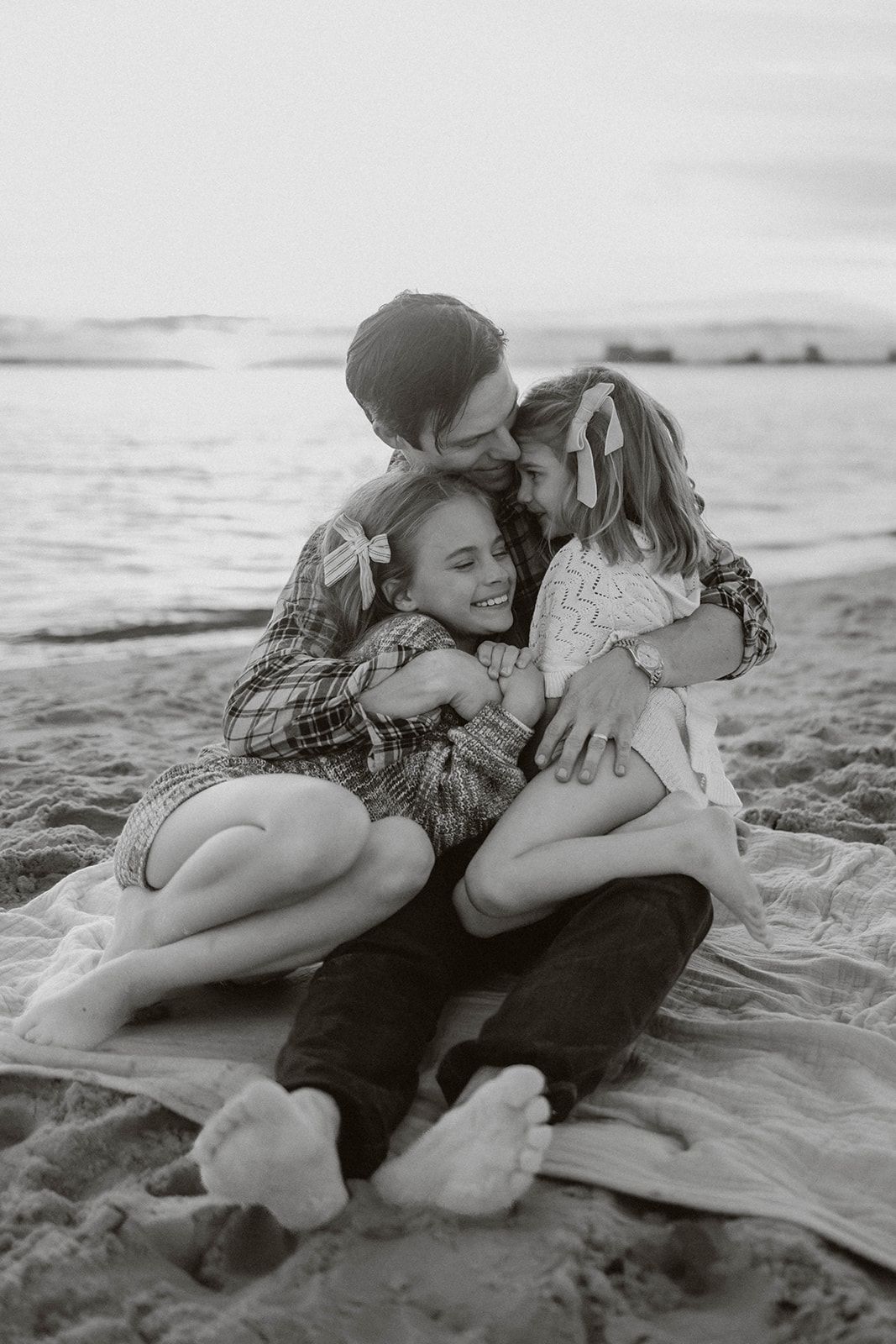 Intimate family moment captured in black and white on beach blanket at sunset.