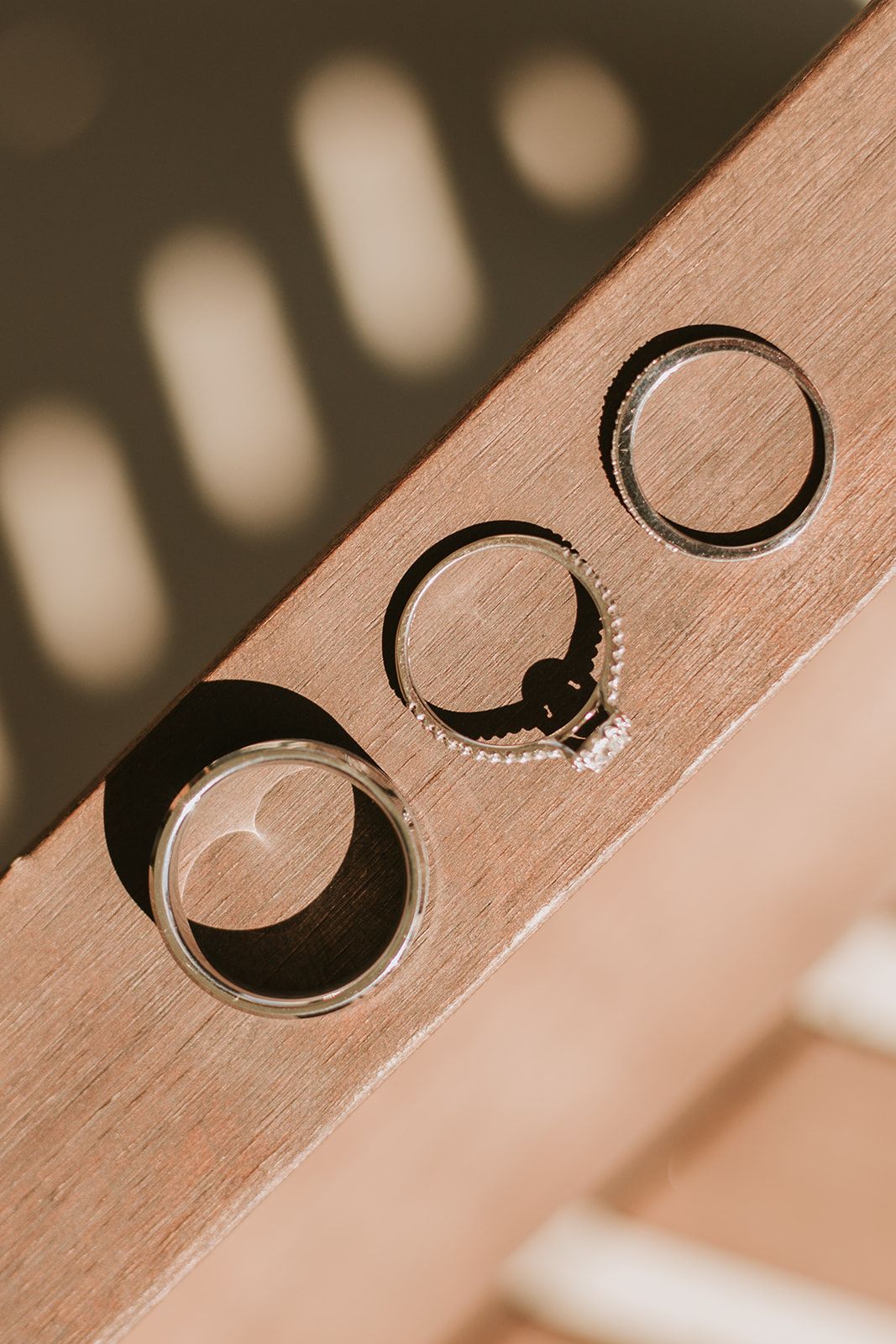 Wedding rings and engagement ring with diamond casting shadows on wooden surface in artistic sepia tones.