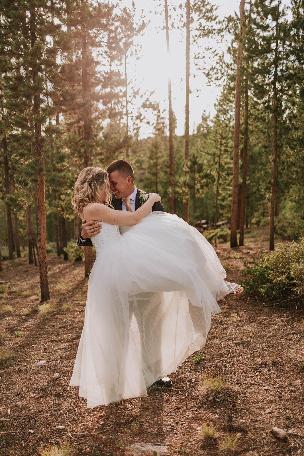 A romantic woodland wedding photo with a flowing white dress captured at sunset among tall pine trees.