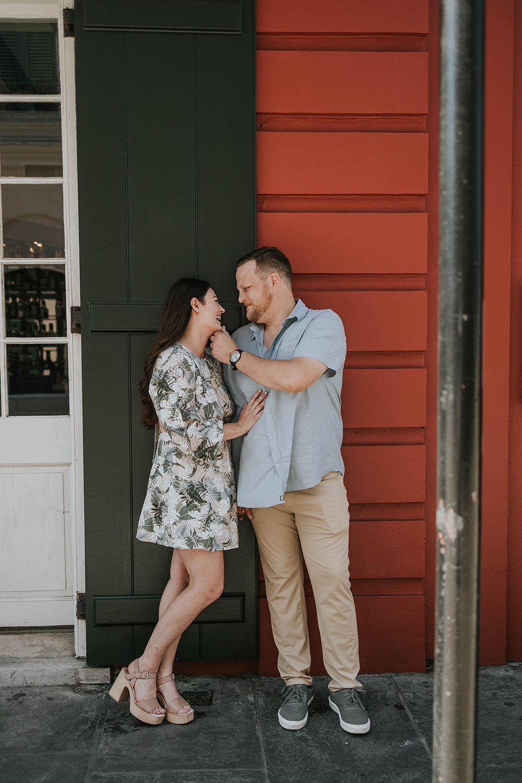 A couple shares a playful moment against a red and green painted building exterior.