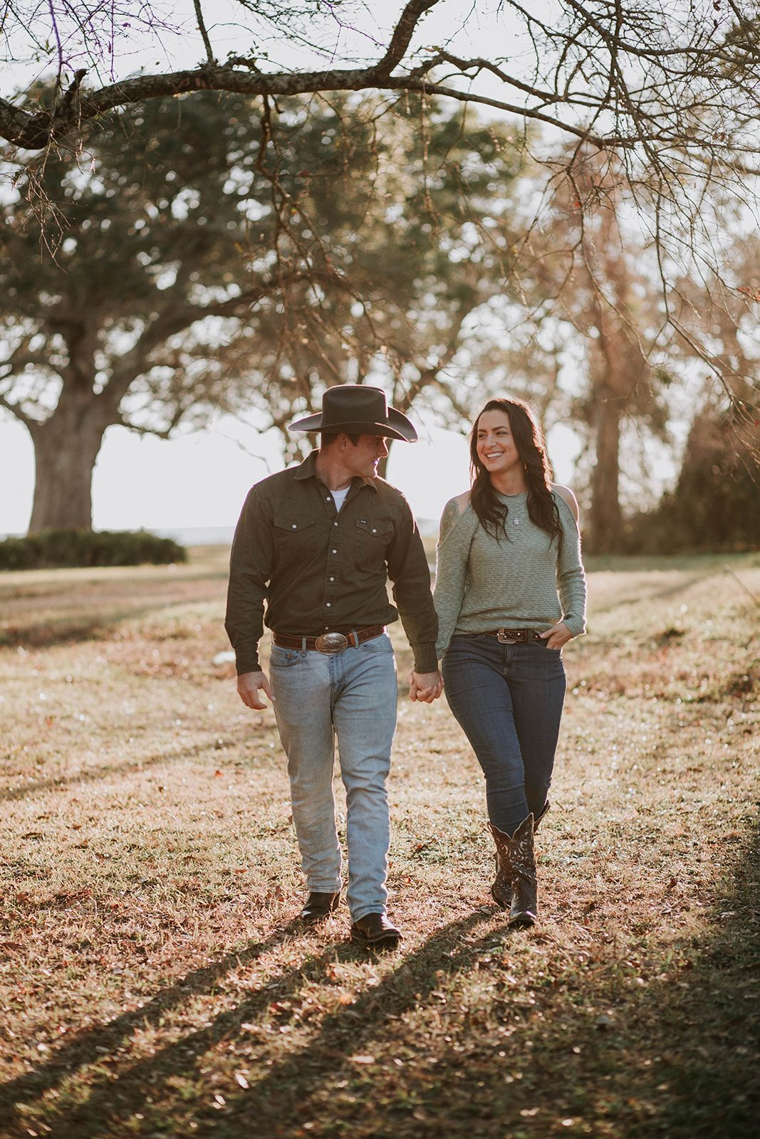 A couple takes a romantic sunset stroll through an autumn landscape wearing western-inspired casual attire.