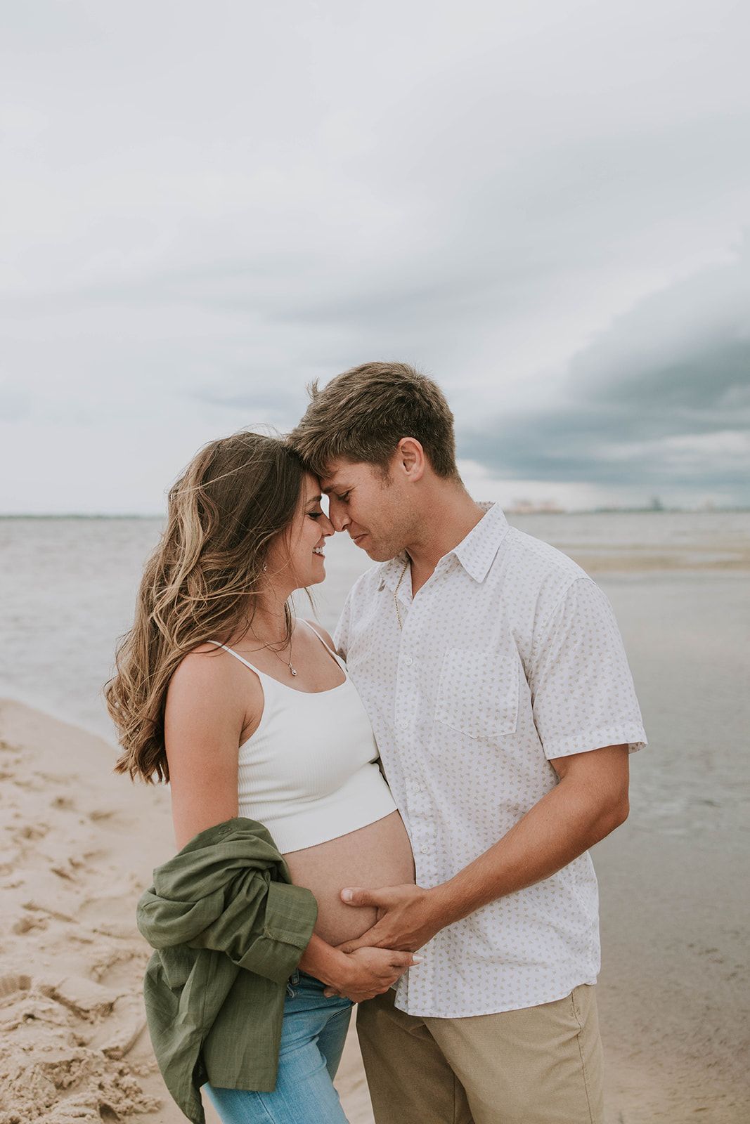 Romantic beach portrait of couple embracing on cloudy day by the ocean.