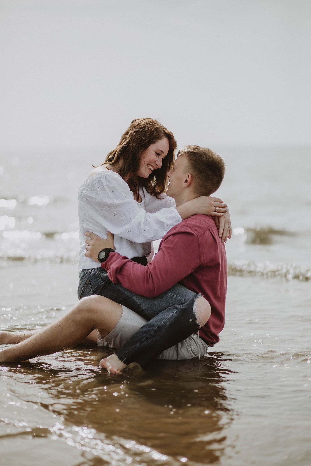 A romantic couple embraces while sitting in shallow ocean waters.