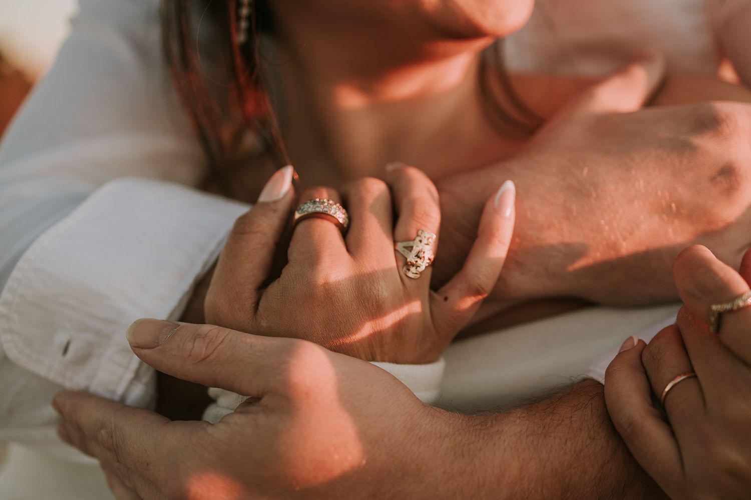 Close up view of hands wearing rings on white fabric in warm sunlight.