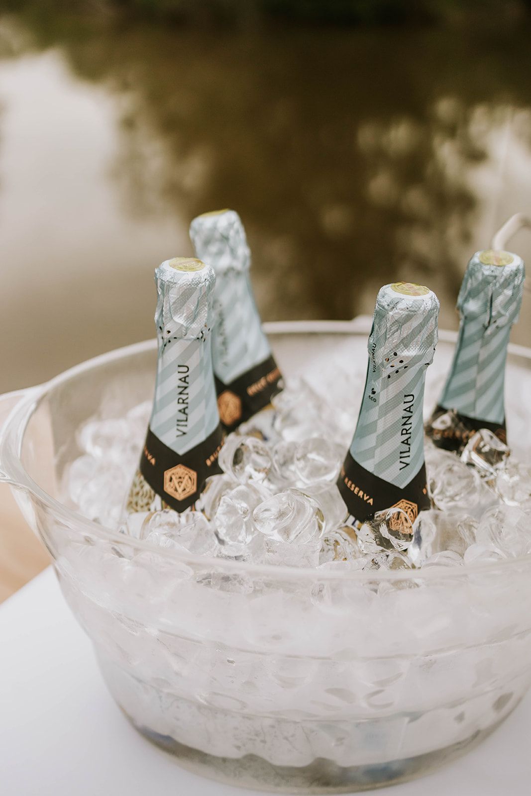 Mini champagne bottles chilling in clear glass bowl filled with ice cubes at what appears to be an event or celebration.