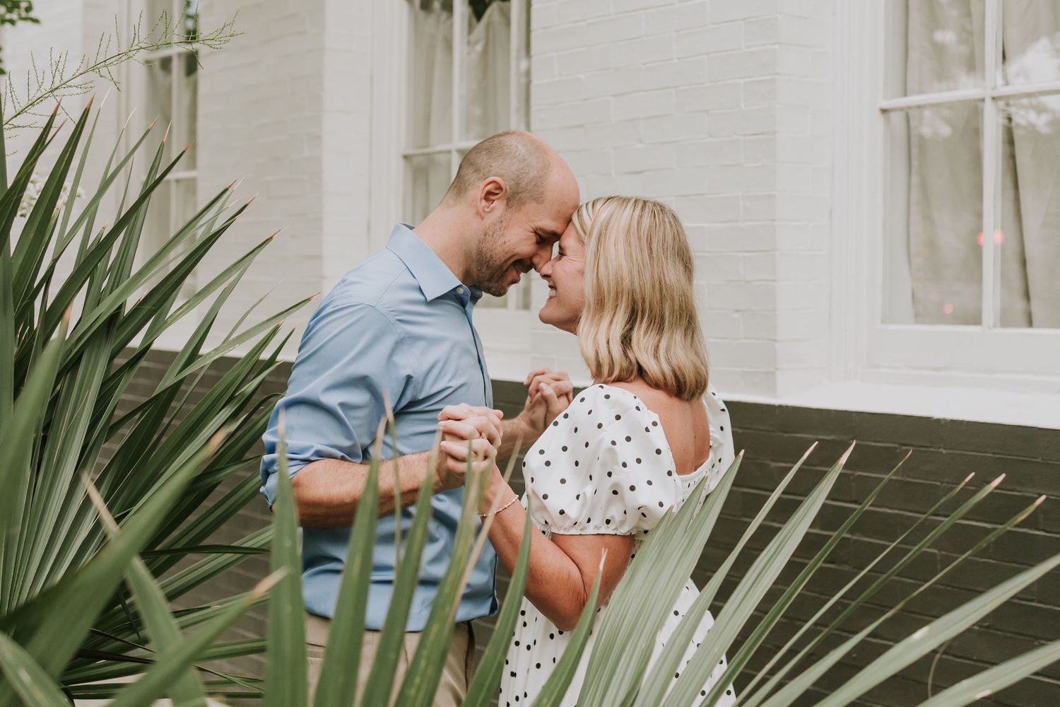 Couple holding hands and touching foreheads in a romantic outdoor engagement photo near tropical plants.