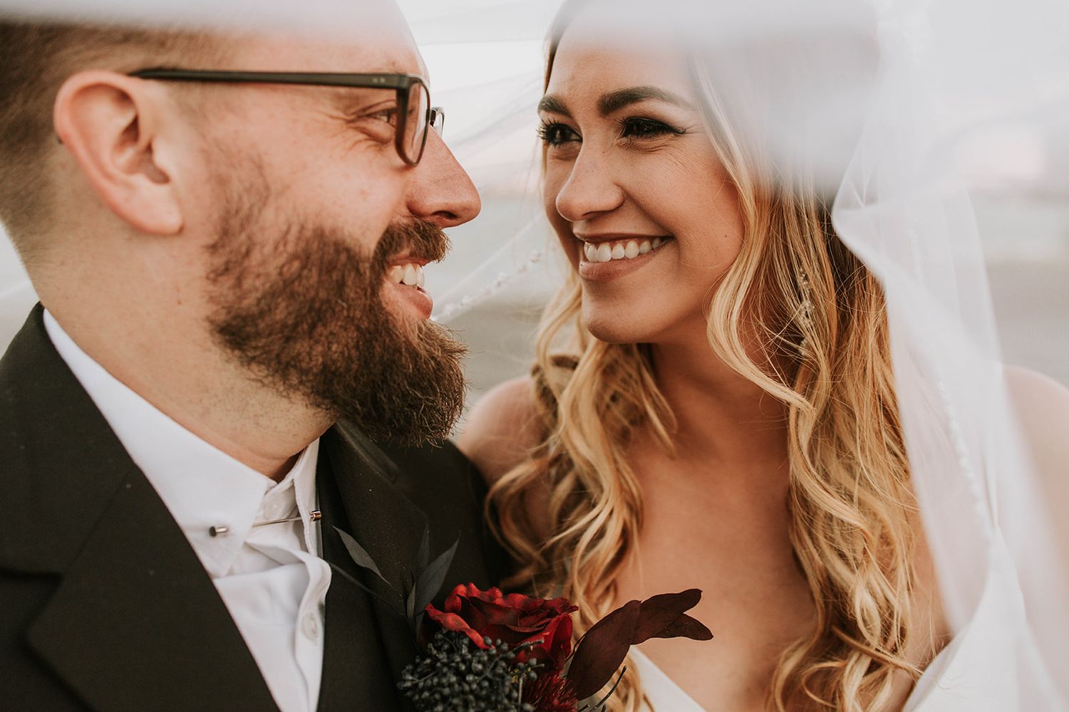 A joyful close up of newlyweds sharing a candid moment on their wedding day with deep burgundy florals.