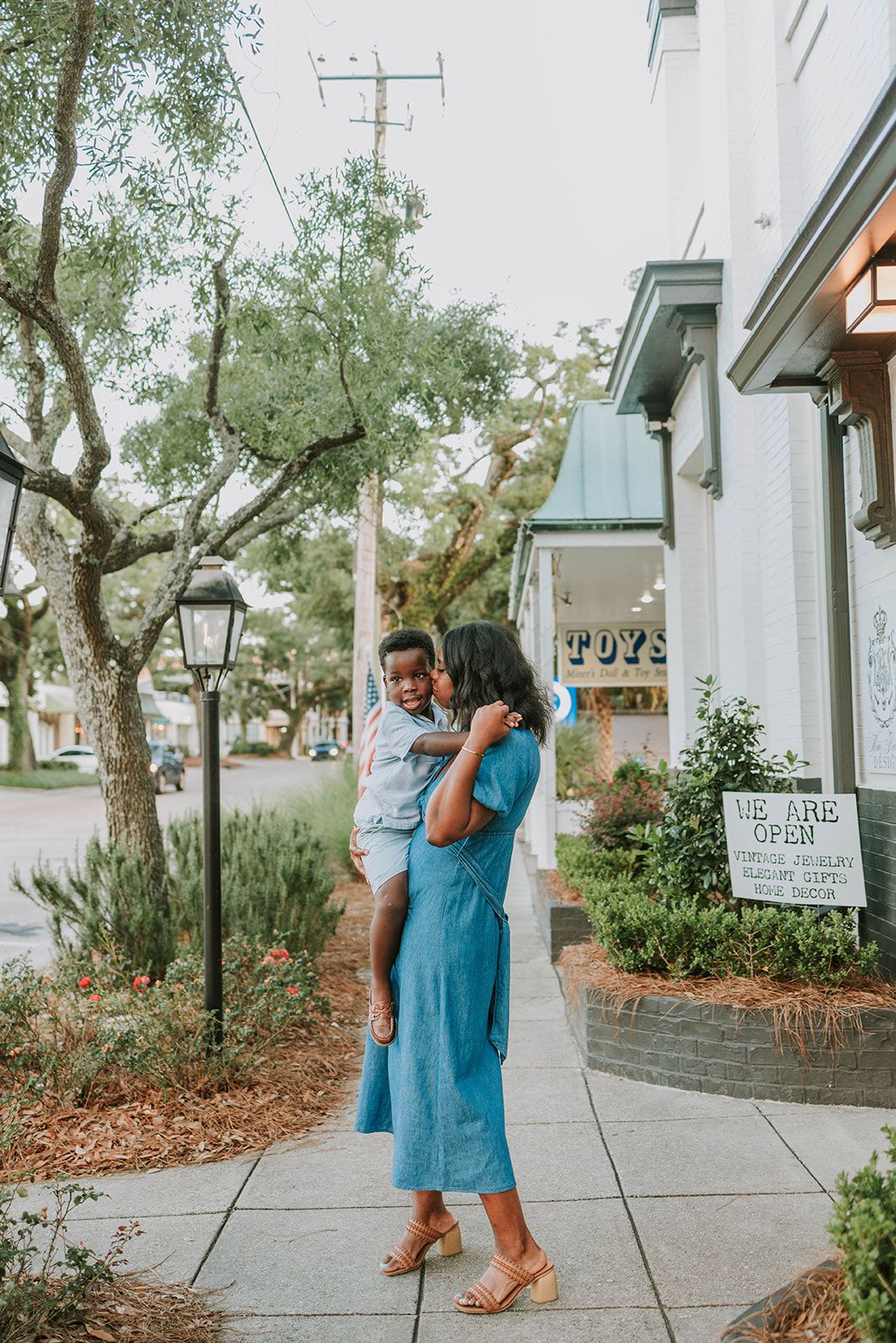 Two people enjoying a stroll on a tree-lined sidewalk outside a charming storefront in an idyllic small town setting.