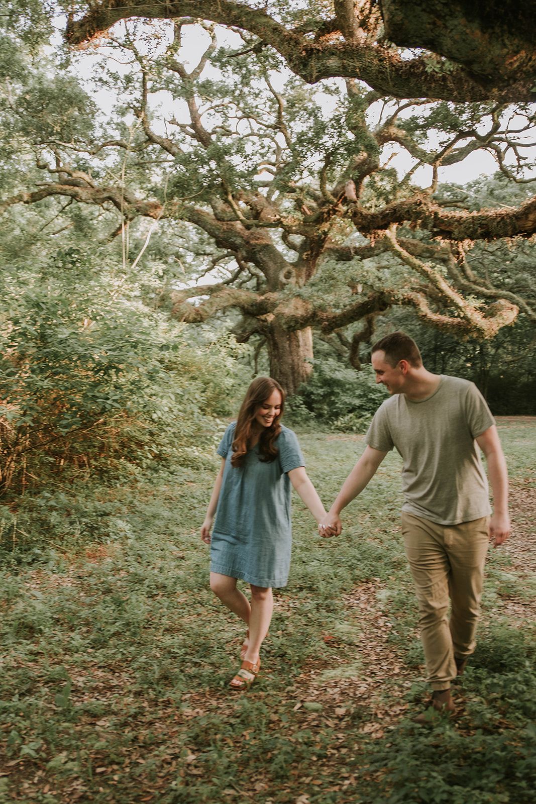 A couple walking hand in hand beneath a majestic twisted tree in a park.