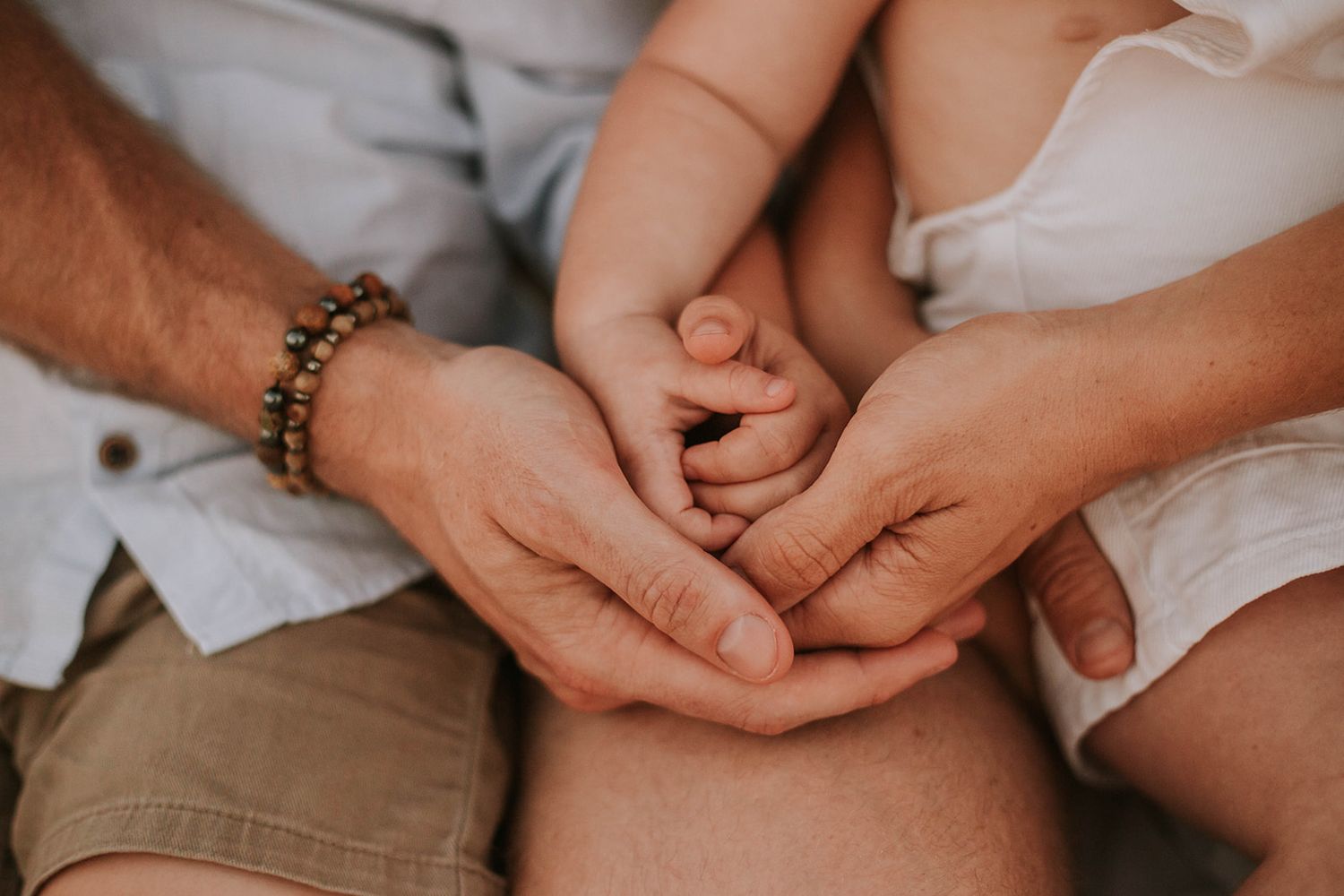Multiple hands join together in a tender moment against a light background.