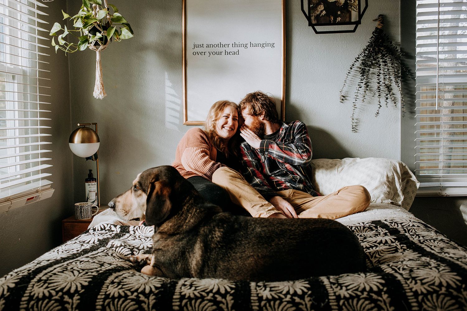 A cozy scene of two people relaxing on a bed with dogs and home decor.