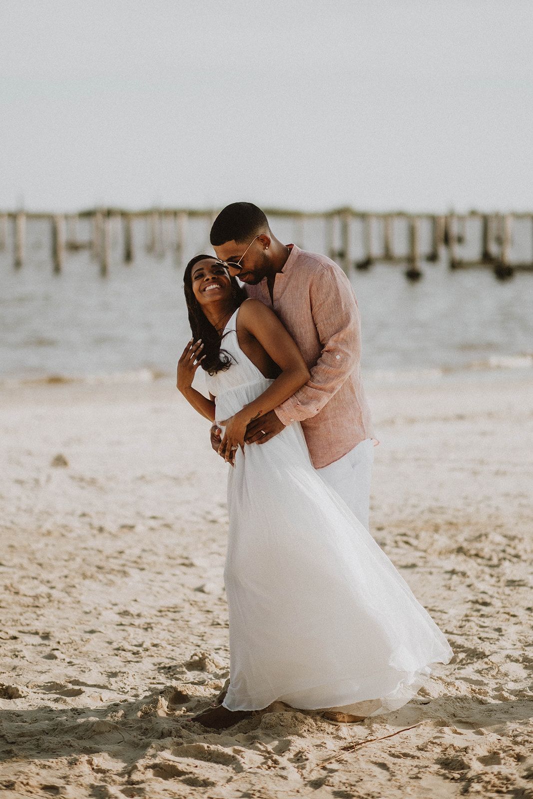 A romantic embrace on a sandy beach at sunset with wooden posts in the background.
