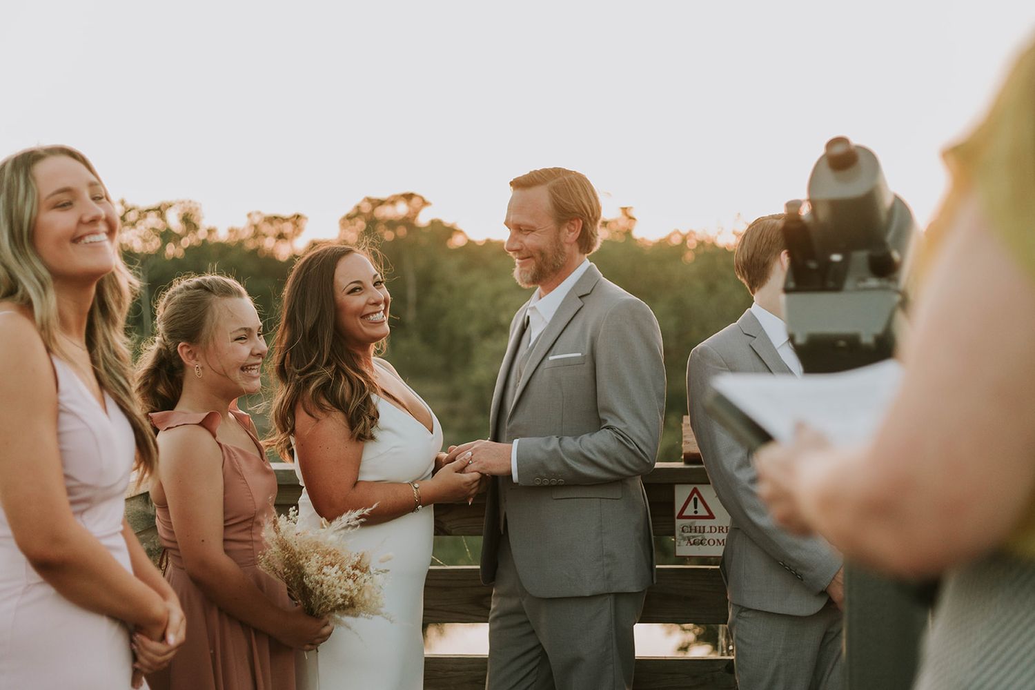 Wedding party gathers outdoors during golden hour sunset at a countryside celebration ceremony.