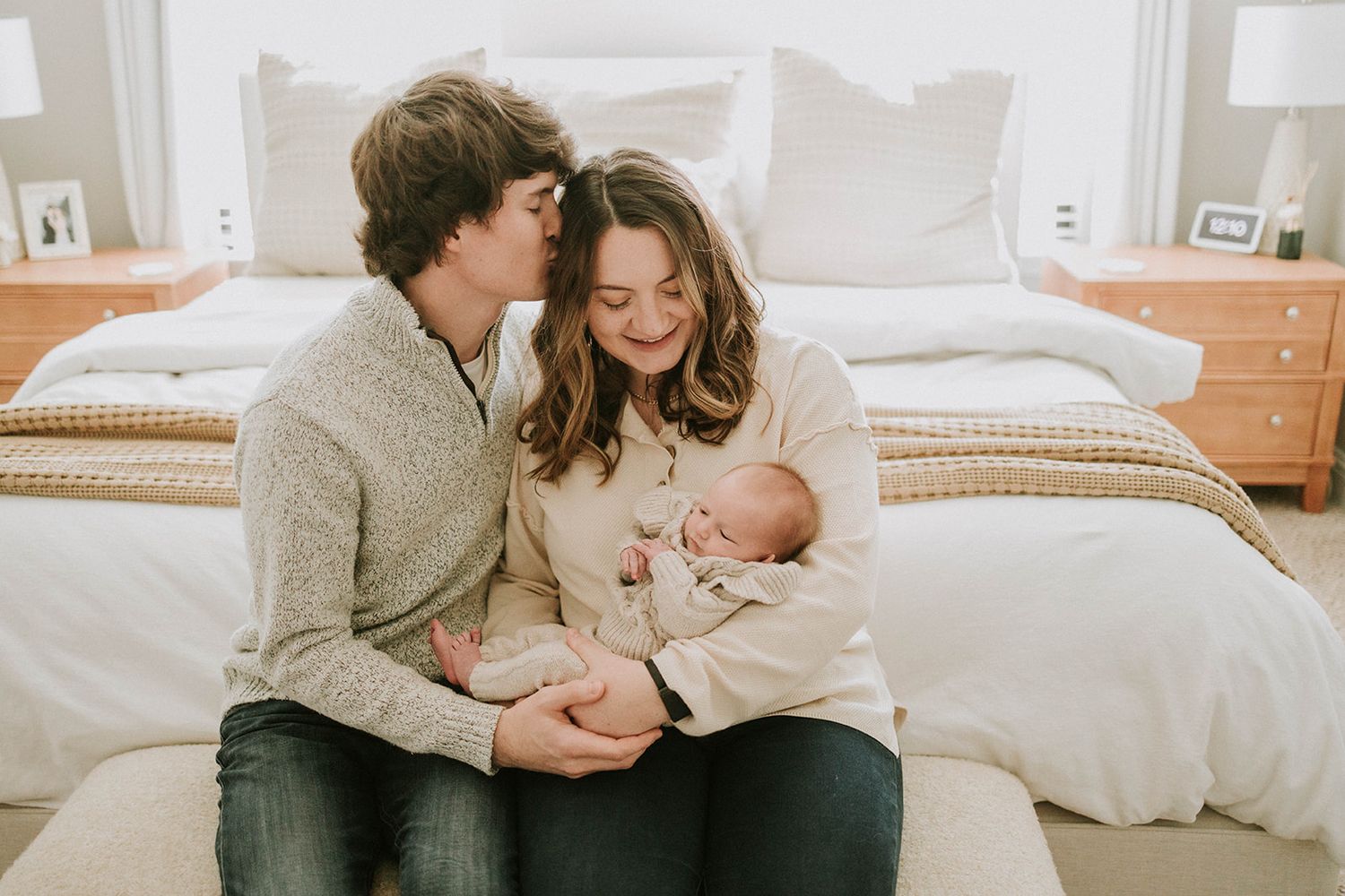 Parents sitting on bed cradling their newborn baby in tender moment at home.