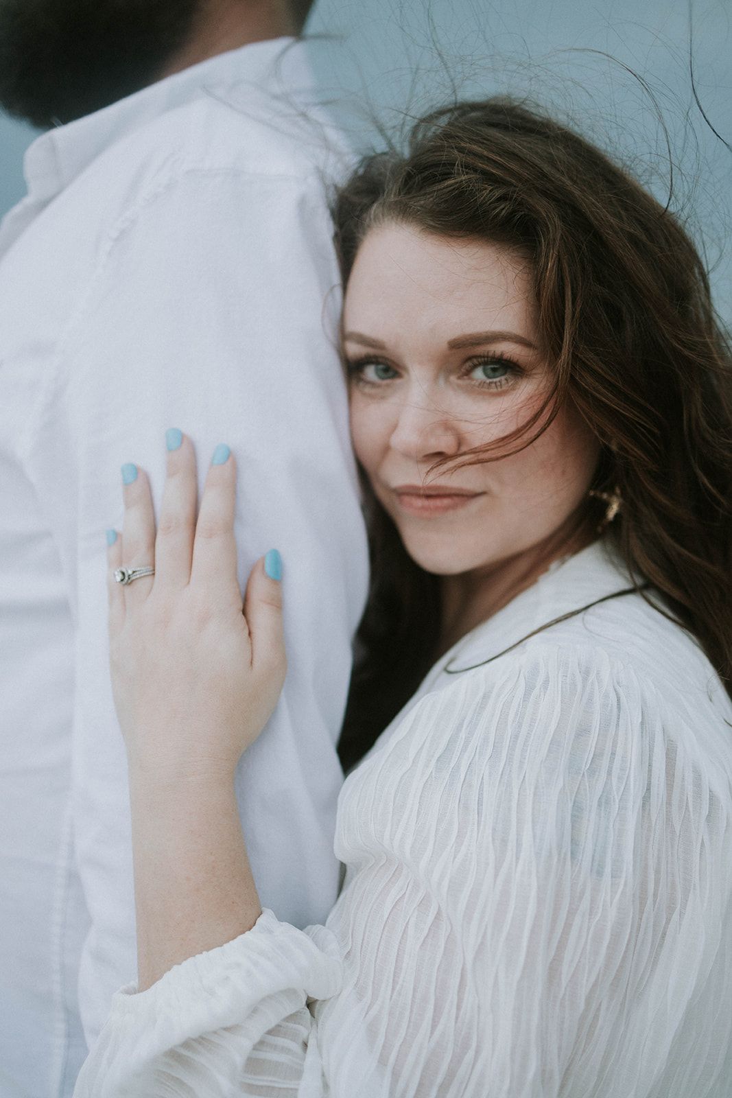 Person in white clothing shown leaning against someone while displaying an engagement ring.